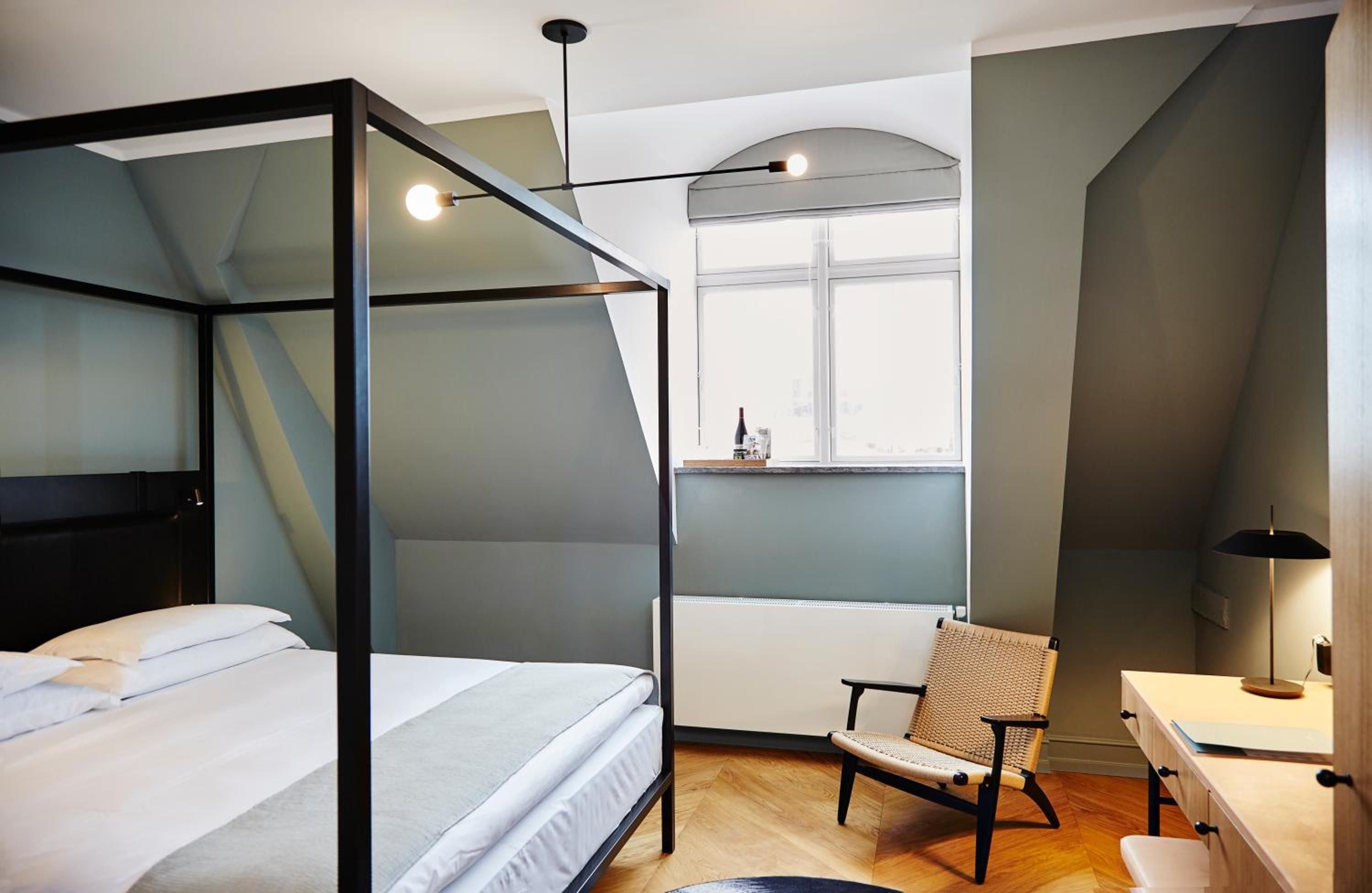 Scandinavian minimalism meets industrial elegance in this thoughtfully appointed guest room, where black steel canopy beds frame crisp white linens beneath soaring ceilings and warm pendant lighting.