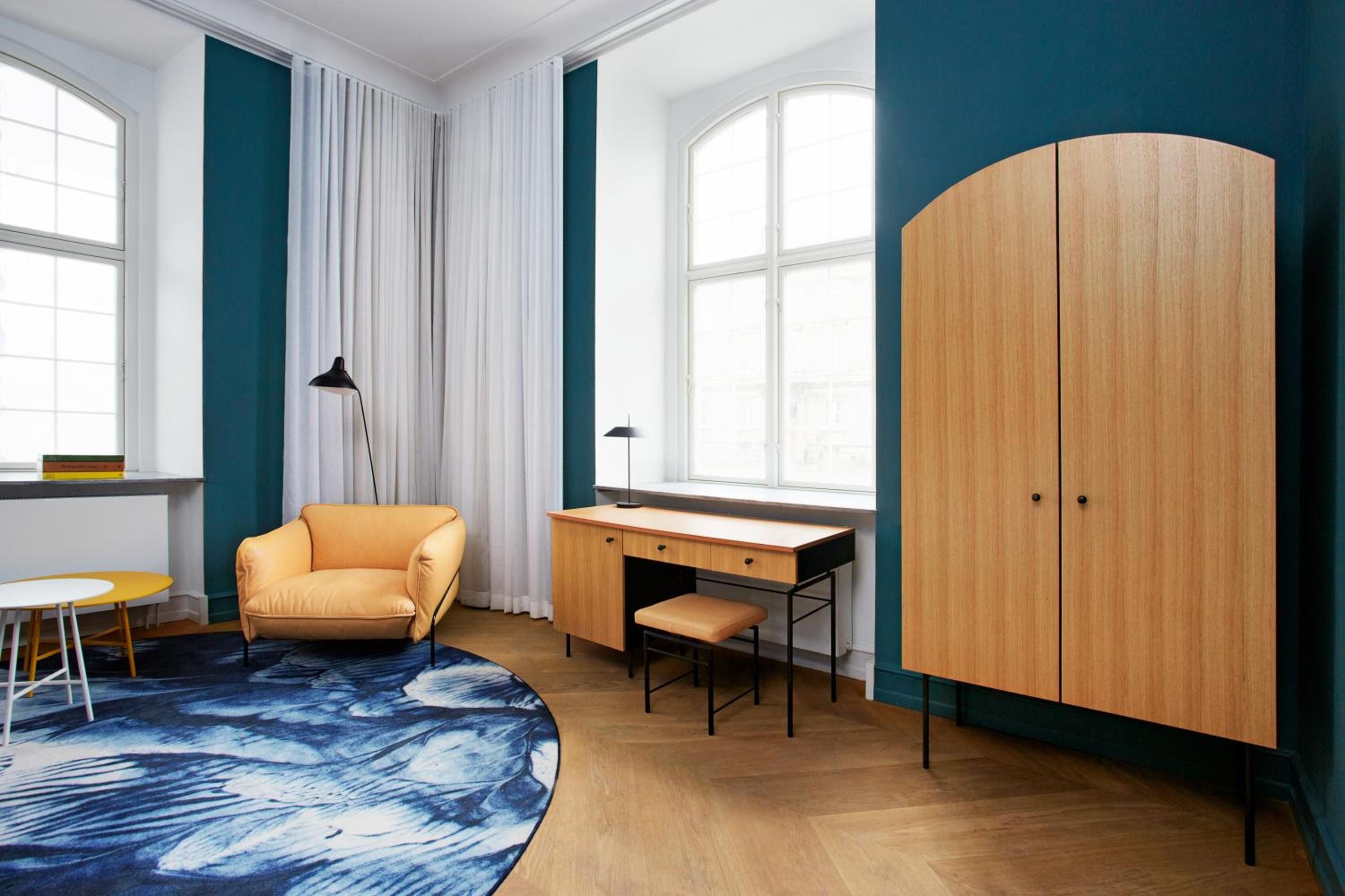 Mid-century furniture in warm oak tones creates an inviting reading nook, while the bold teal accent wall adds contemporary Danish flair to this thoughtfully appointed guest room.