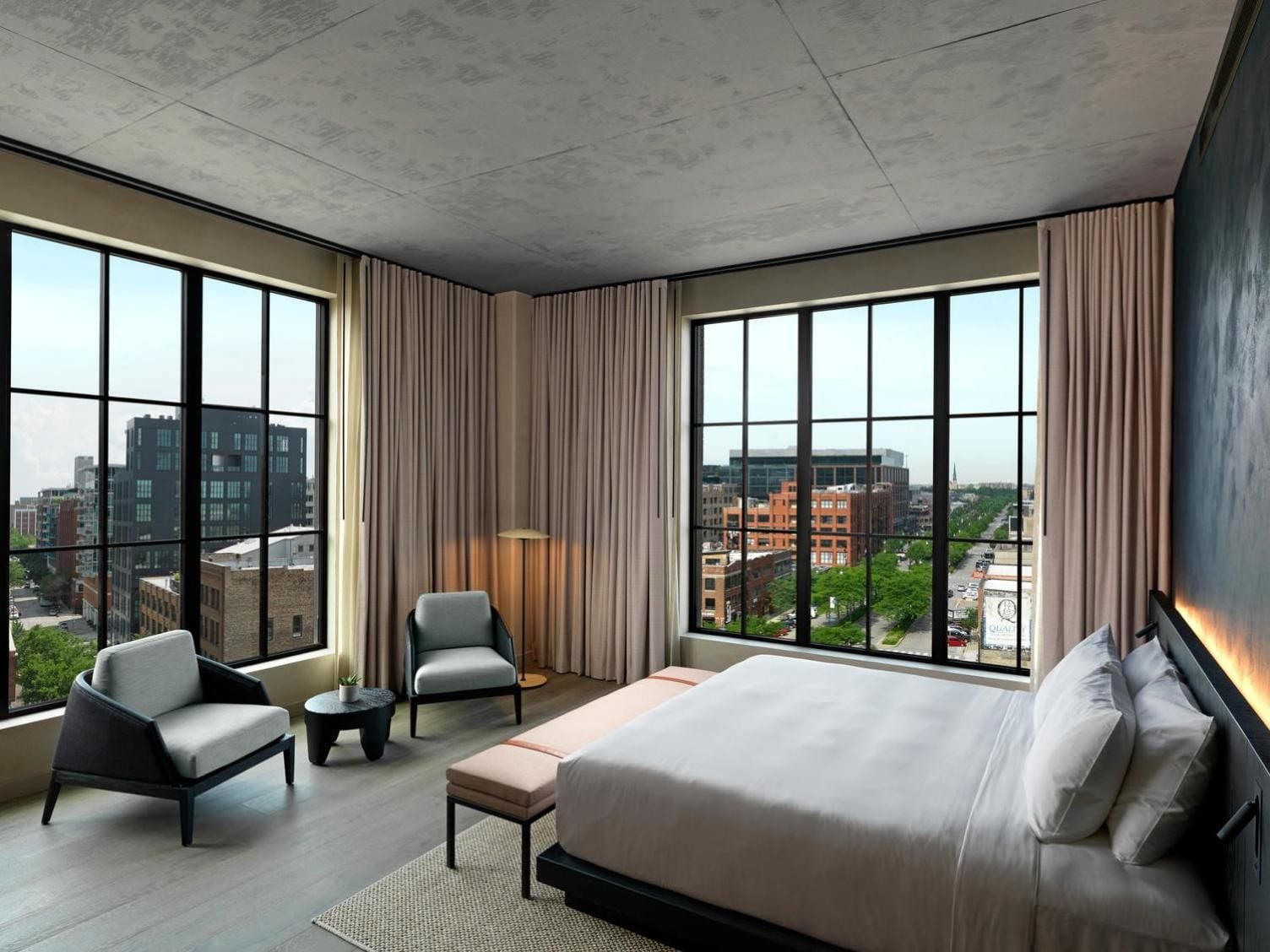 Floor-to-ceiling windows frame Chicago's urban landscape from this corner suite, where concrete ceilings and warm curtains create an intimate cocoon above the bustling streets.