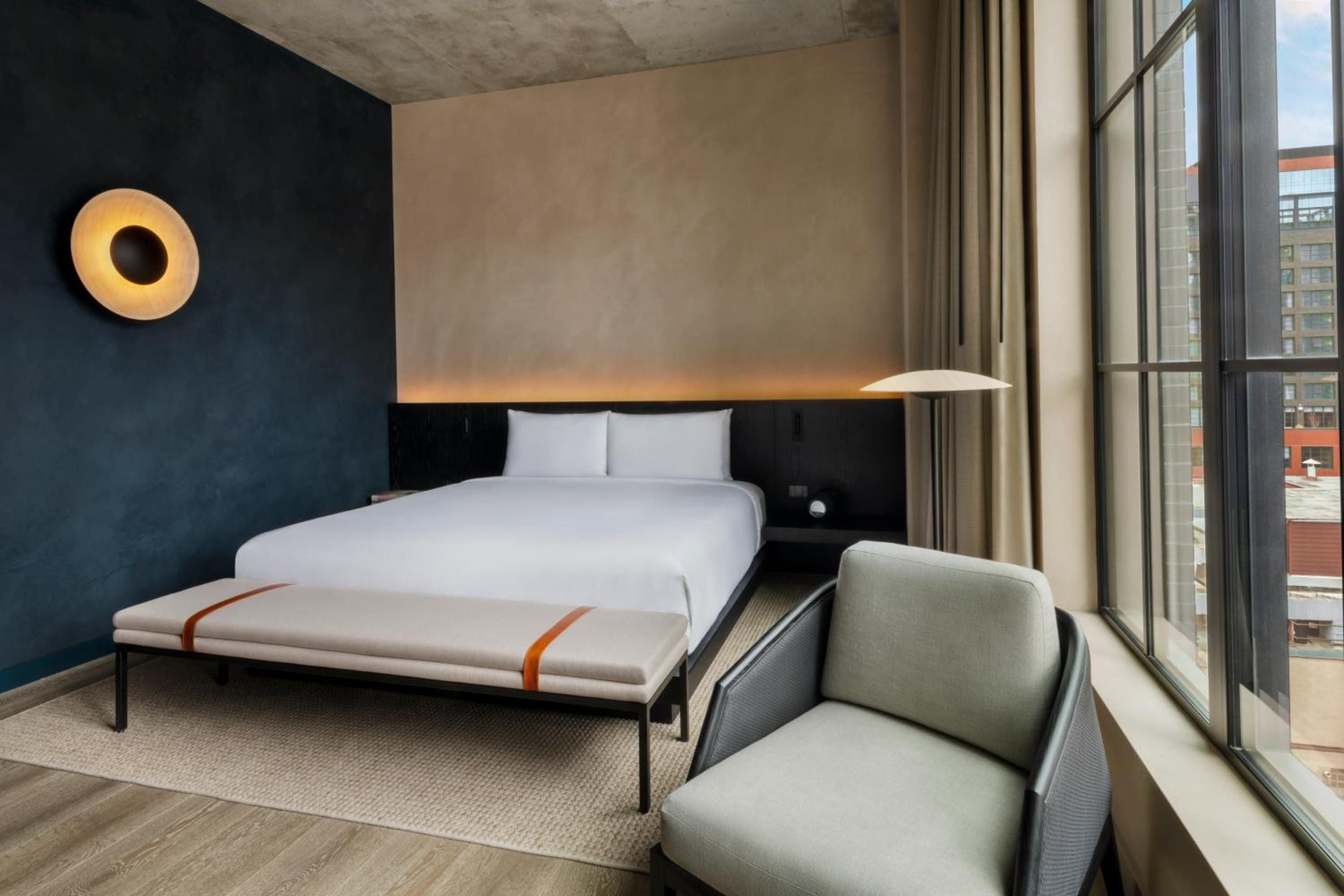 Warm wood floors meet midnight blue walls in this sophisticated guest room, where geometric lighting and neutral linens create an intimate urban sanctuary above Chicago's streets.