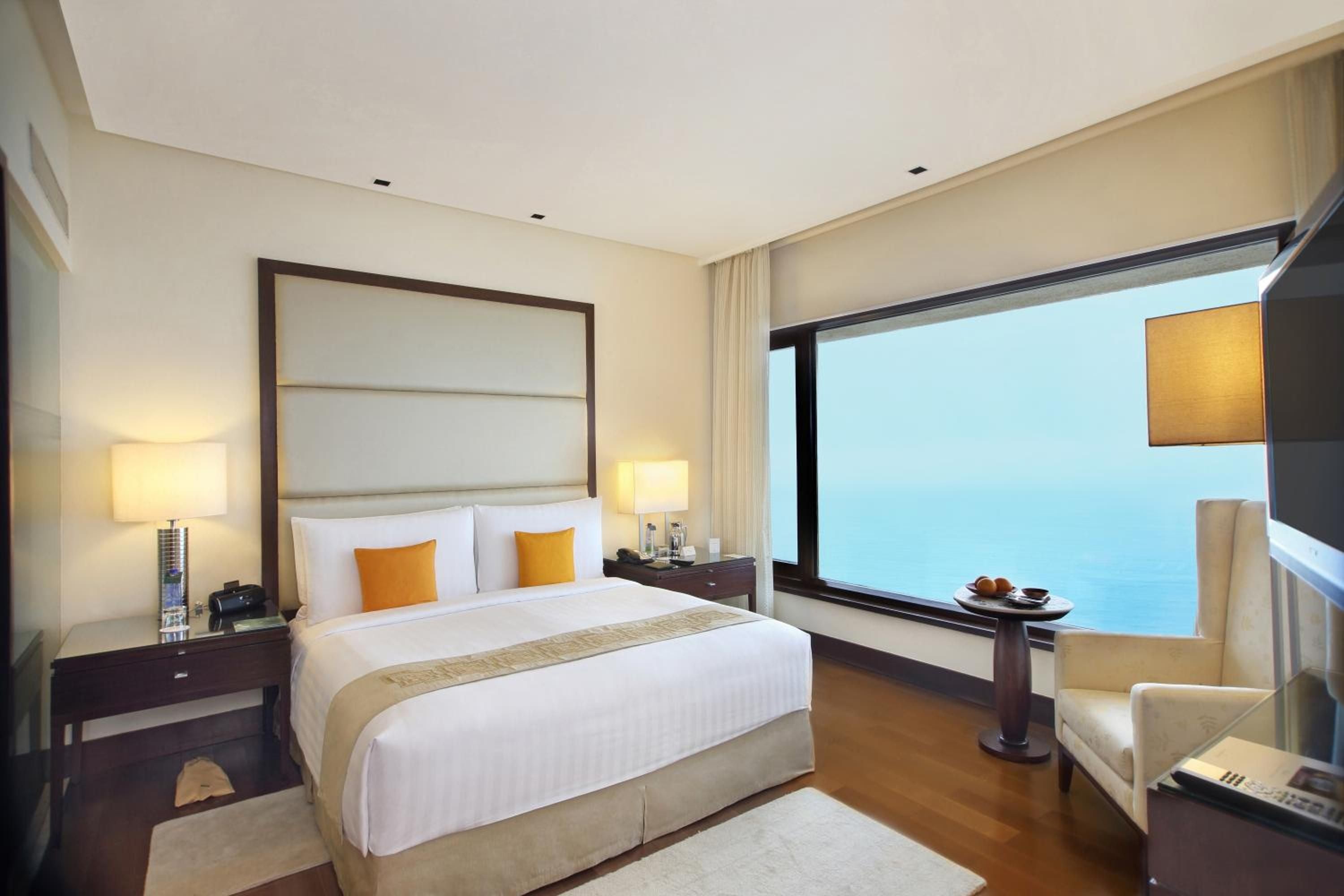 Floor-to-ceiling windows frame endless ocean vistas while warm amber lighting and rich wood finishes create an intimate sanctuary high above the coastline.