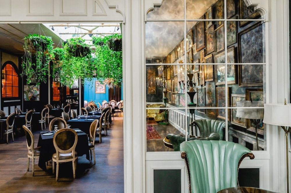 Curated artwork climbs salon-style walls while intimate dining spaces unfold beyond French doors, creating an enchanting blend of gallery sophistication and Southern hospitality.
