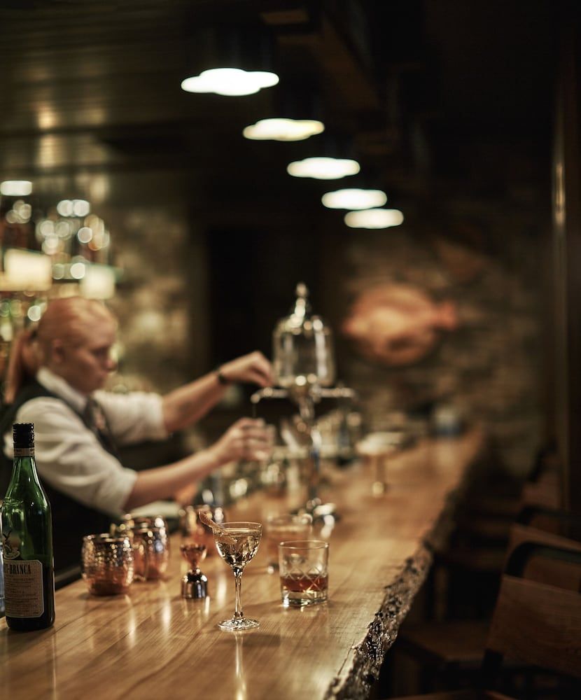 Crystal stemware catches amber light as the master bartender works his craft, transforming this intimate wood-paneled sanctuary into New Orleans' most refined drinking den.