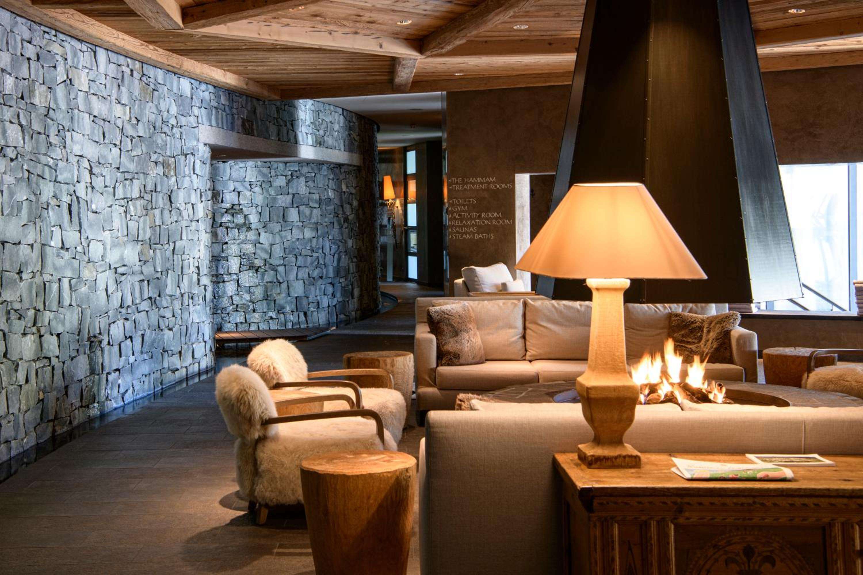 Stone walls meet exposed timber beams in the spa's relaxation lounge, where crackling fires and sheepskin throws create alpine sanctuary vibes beneath warm lamplight.