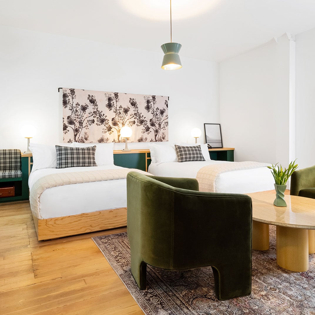 Plaid cushions and botanical wallpaper create intimate charm in this thoughtfully designed twin room, where sage green accents and warm wood floors invite quiet moments.