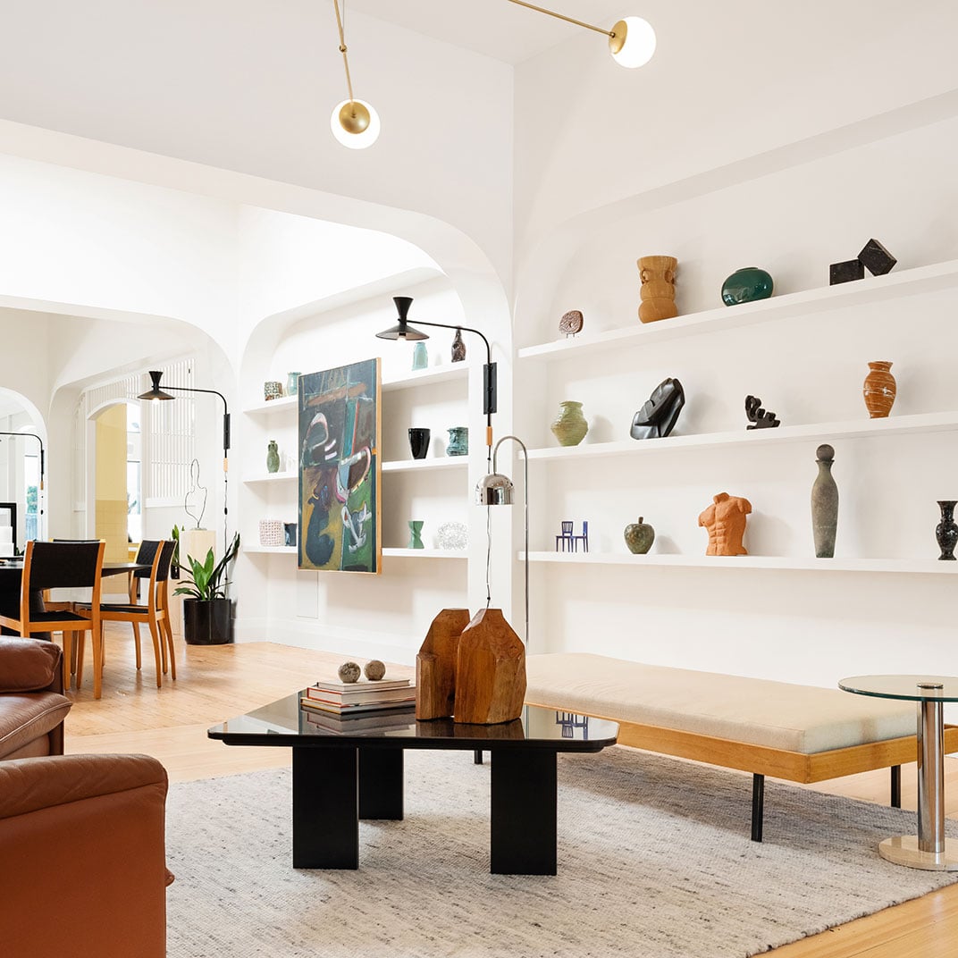 Sculptural white shelving cradles ceramic treasures while brass pendants cast warm pools of light across this sophisticated lounge's curved archways and rich leather seating.