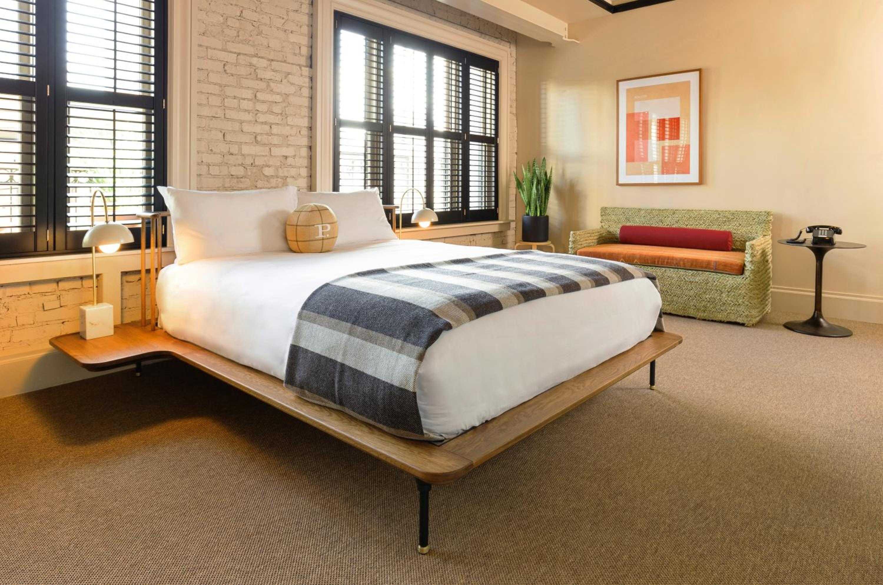Mid-century modern meets industrial chic in thoughtfully appointed rooms featuring walnut platform beds, exposed brick walls, and sculptural pendant lighting that creates an intimate urban sanctuary.