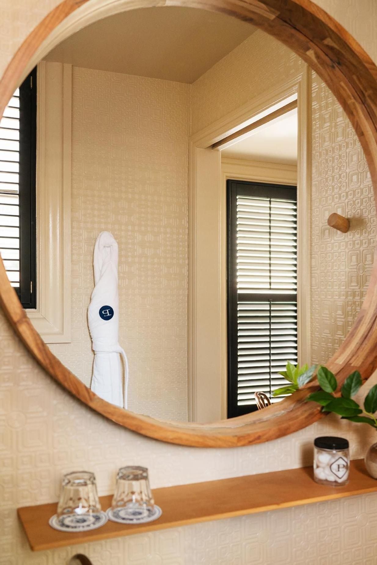 Warm wood-framed mirrors reflect geometric wallpaper and crisp linens, while thoughtfully placed glassware creates an intimate, residential feel in guest quarters.