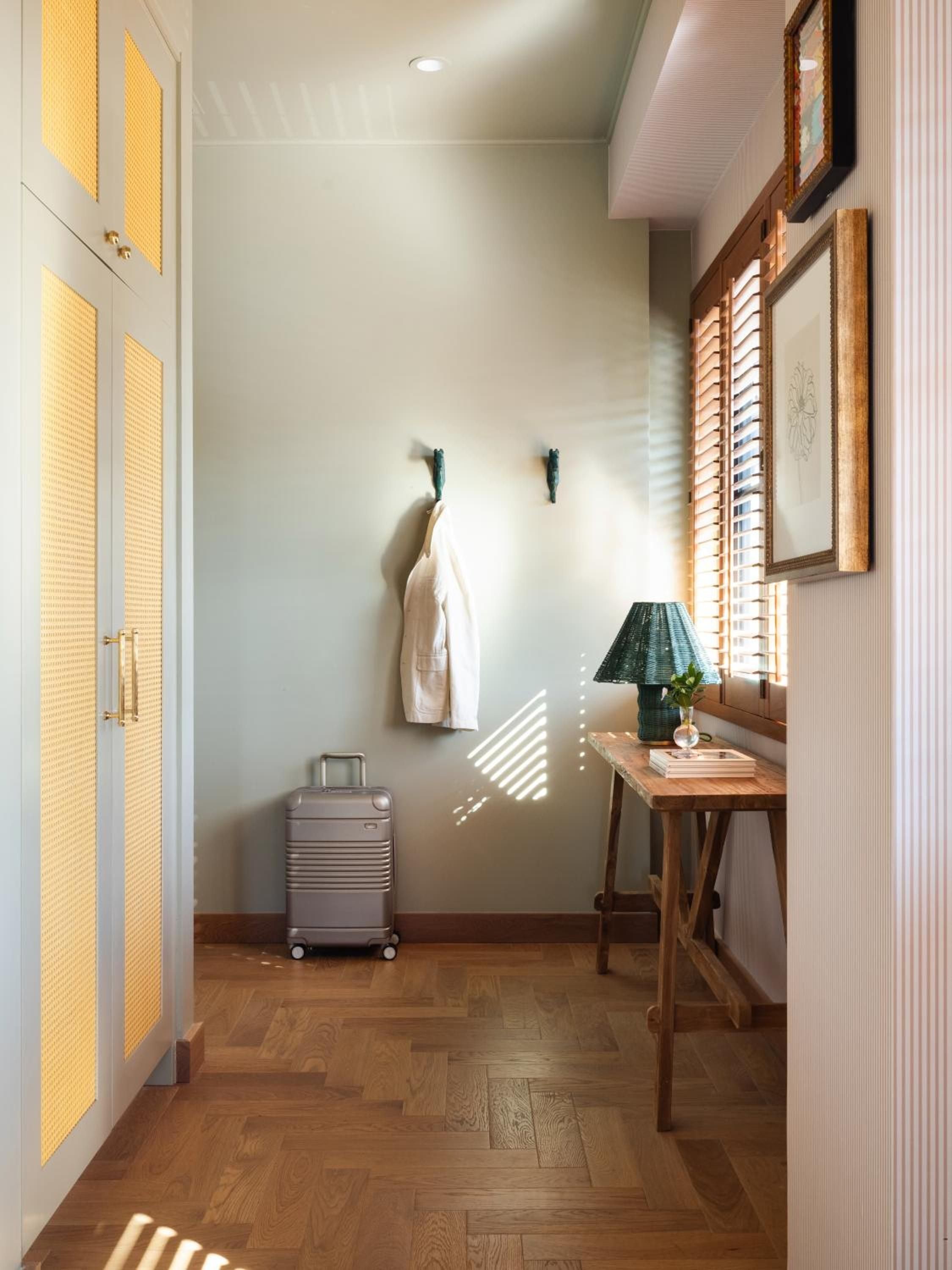 Warm afternoon light filters through wooden shutters, casting geometric shadows across this thoughtfully appointed guest room where vintage suitcases and cane-backed furniture create an effortlessly sophisticated atmosphere.
