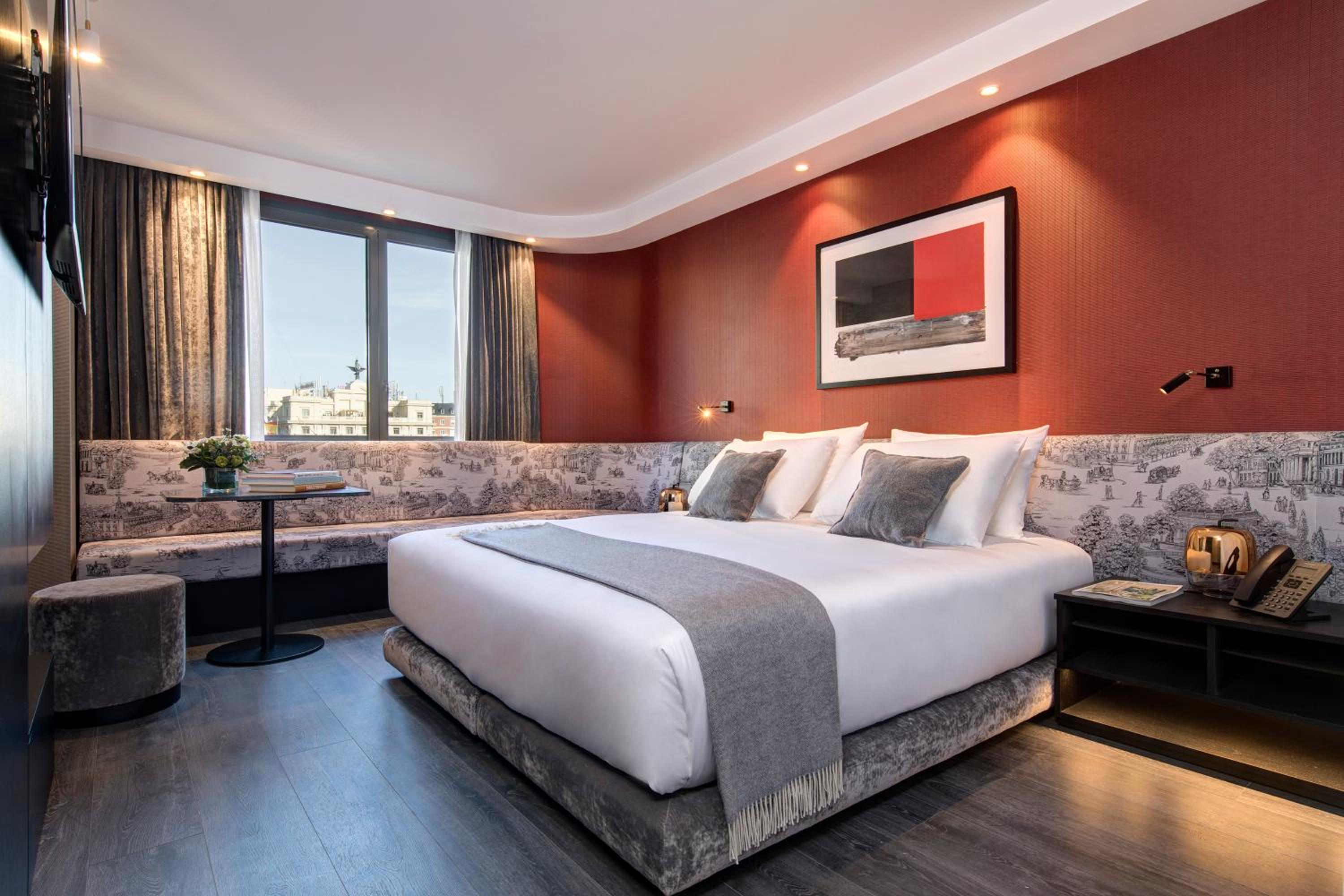 Crimson accent walls and custom toile upholstery create intimate sophistication in this corner suite, where Parisian-inspired details meet contemporary Madrid style.