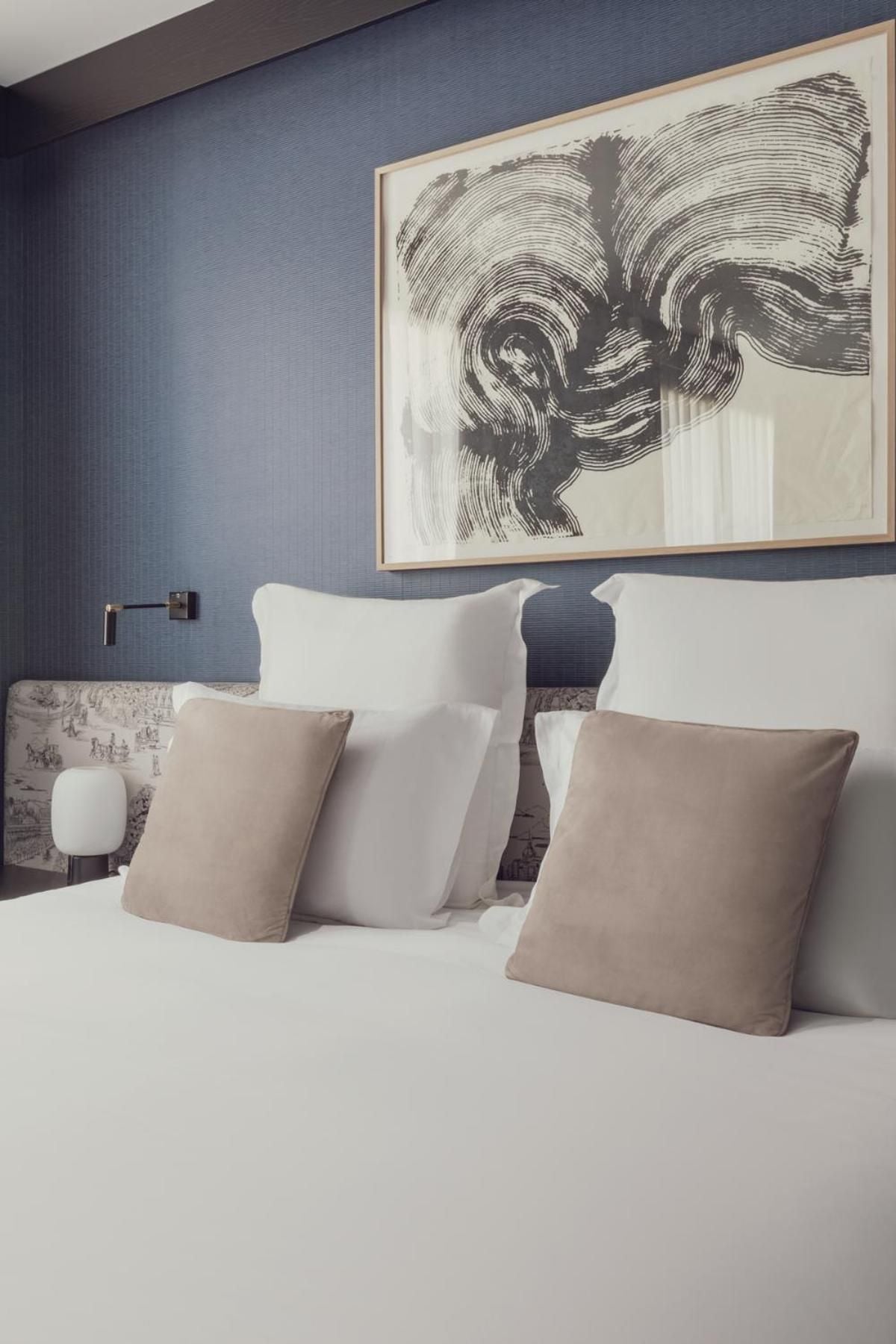 Swirling brushstrokes above the bed echo movement and energy, while neutral linens and warm sconces create an intimate sanctuary of contemporary sophistication.