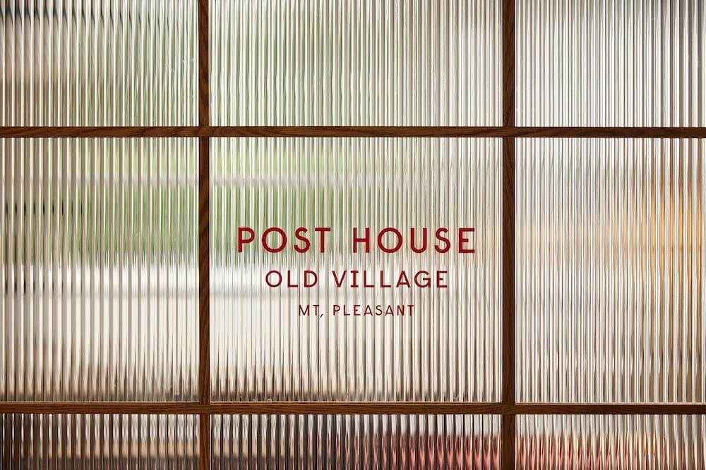 Fluted glass panels filter golden light through Post House's entrance, creating an intimate sense of arrival while offering glimpses of the lush gardens beyond.