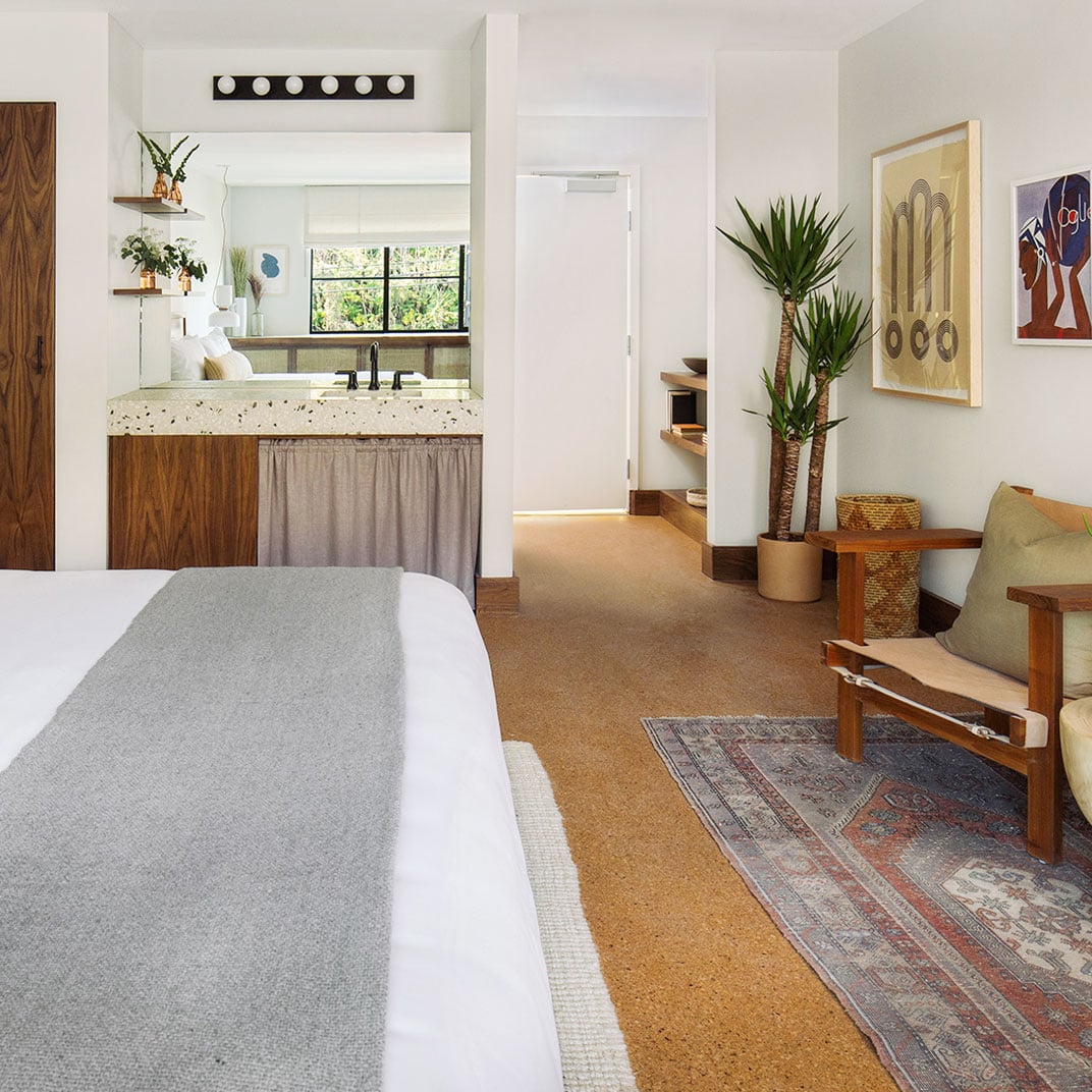 Cork floors warm the thoughtfully curated guest rooms, where mid-century furniture mingles with vintage rugs and palm trees stretch toward white-washed walls adorned with local art.