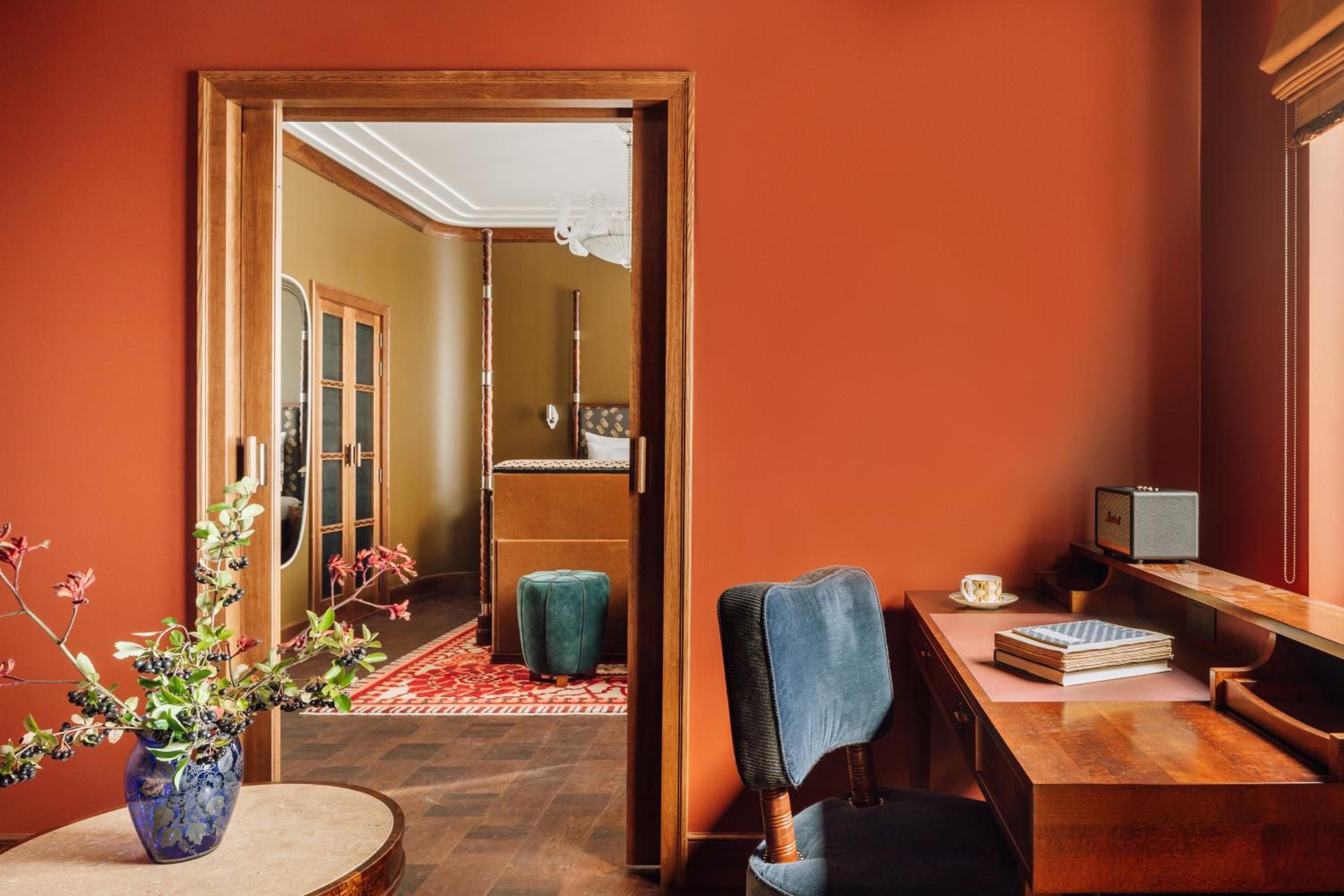 Warm terracotta walls embrace a thoughtfully curated study, where vintage blue velvet meets rich wood furnishings and carefully arranged books invite lingering moments of quiet contemplation.