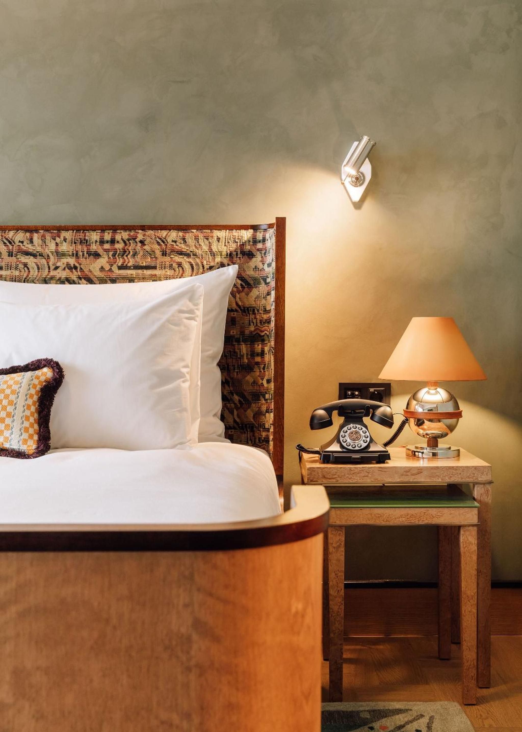 Warm light from a vintage table lamp illuminates the retro rotary phone and textured headboard, creating an intimate corner where mid-century charm meets modern comfort.