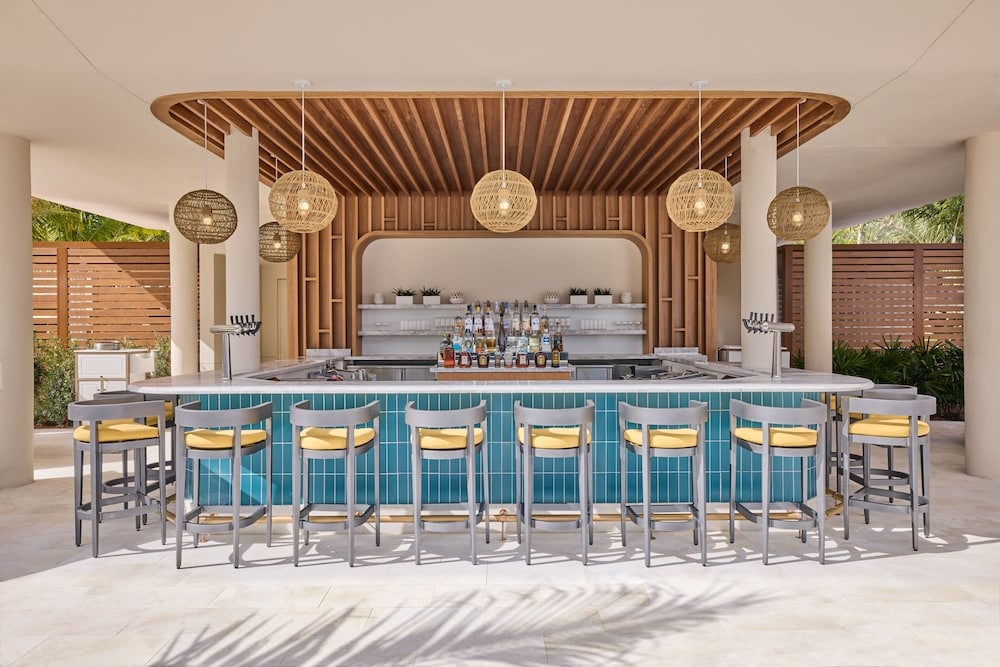 Woven pendant lights cast golden shadows over the turquoise-tiled swim-up bar, where natural wood slats create an intimate canopy for sunset cocktails poolside.