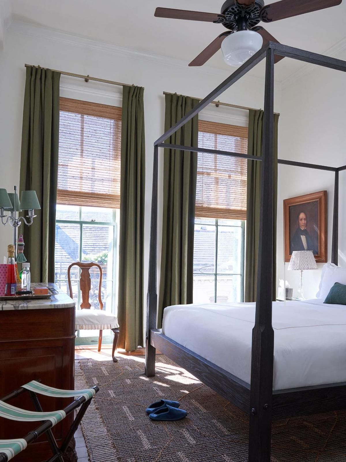 Morning light filters through bamboo shades in this canopy-bed guest room, where olive curtains and warm wood furnishings create an inviting Southern sanctuary.