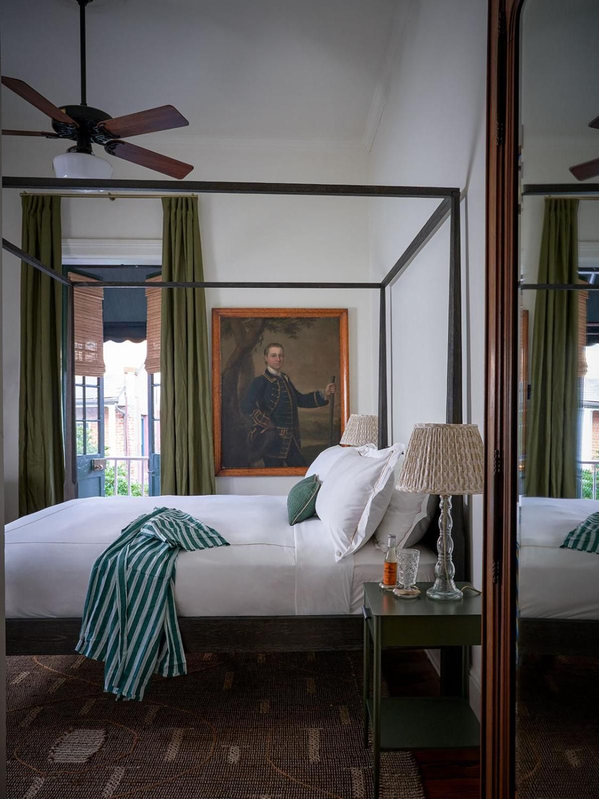 Steel four-poster beds and emerald velvet curtains create colonial elegance beneath soaring ceilings, while historic portraits add gravitas to these sophisticated French Quarter suites.