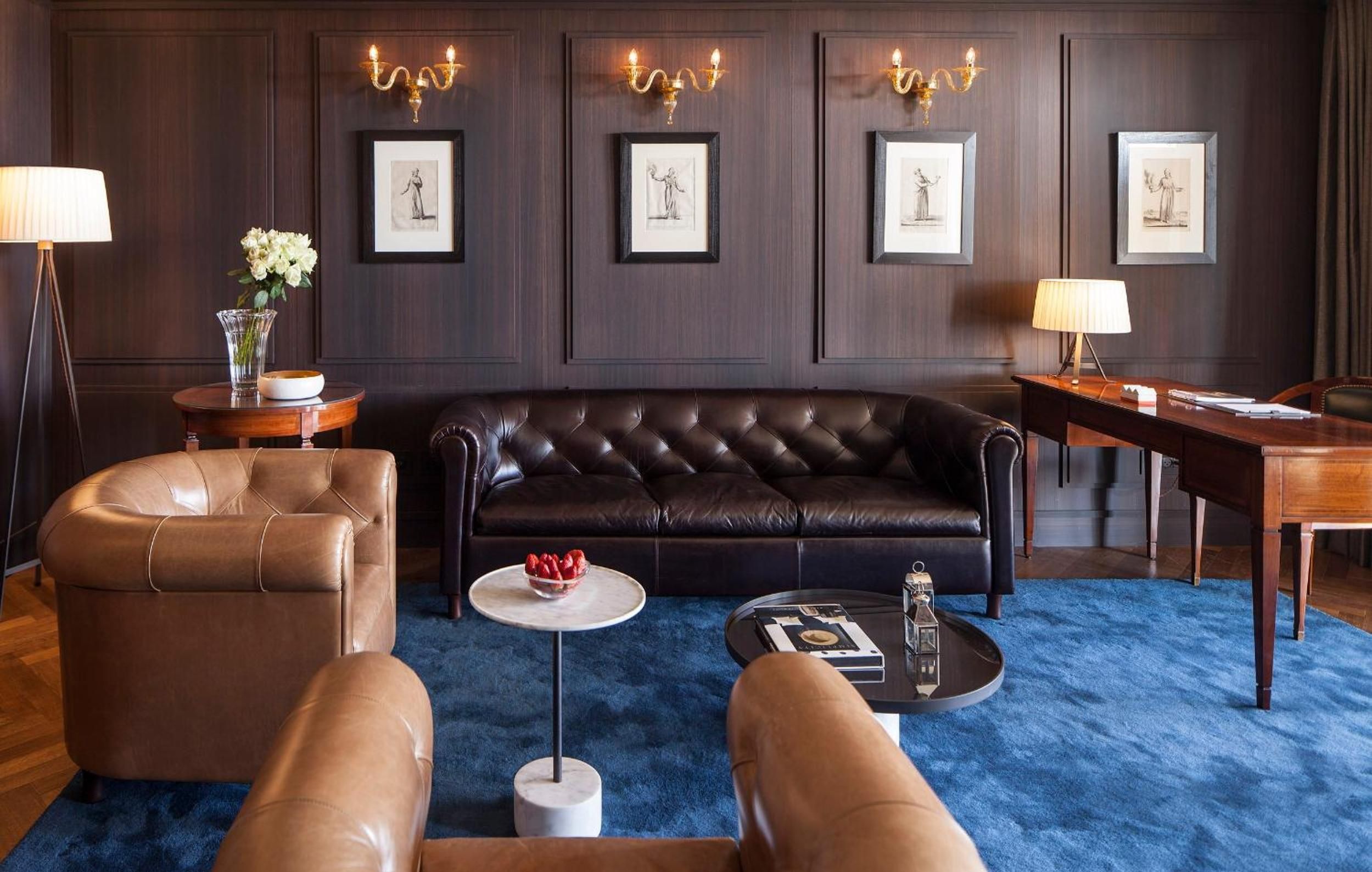 Rich walnut paneling and brass sconces create an intimate library atmosphere, while leather Chesterfield seating and a sapphire rug invite lingering conversations over coffee.