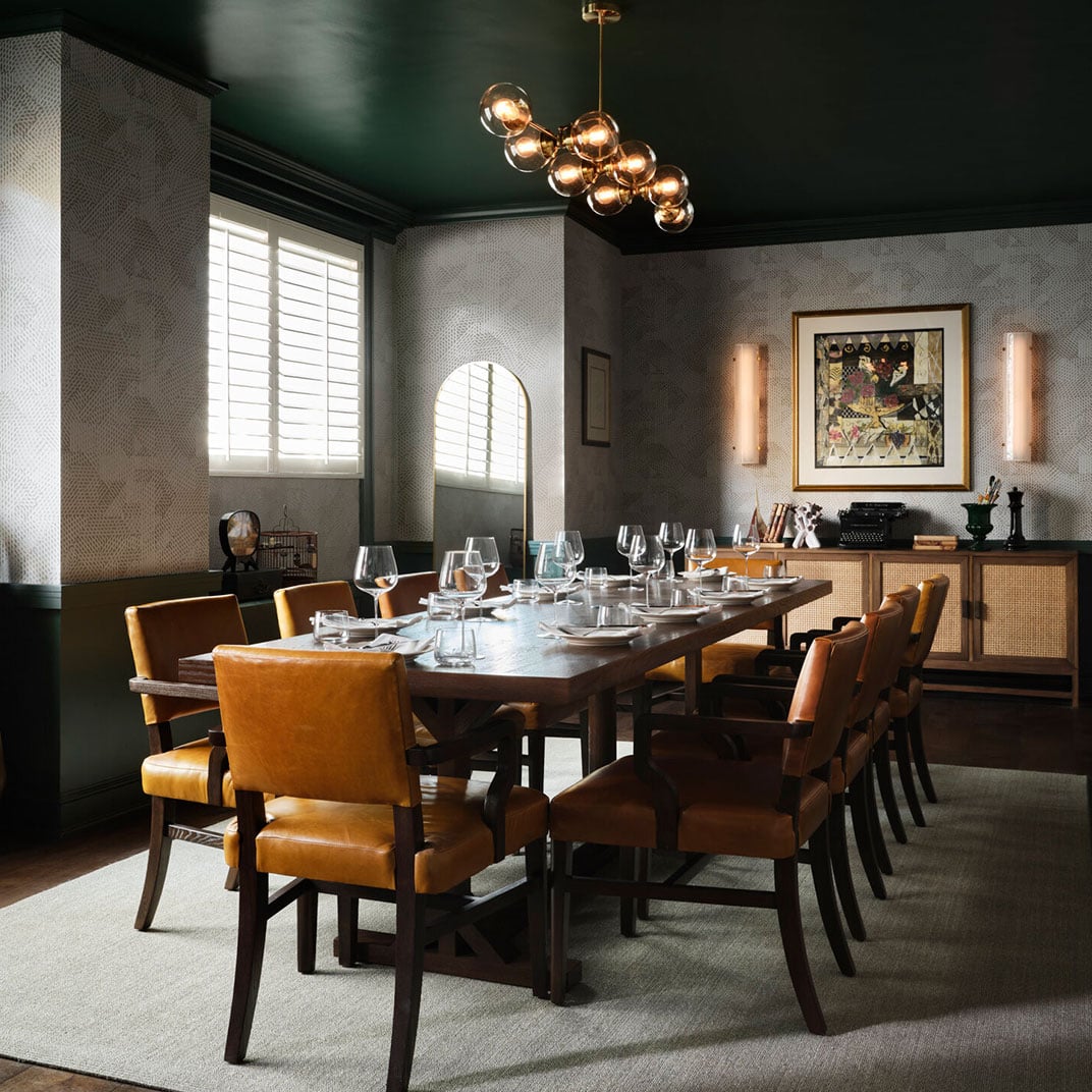Amber leather chairs and golden orb lighting create an intimate dining sanctuary, where textured grasscloth walls and arched windows frame sophisticated culinary conversations.