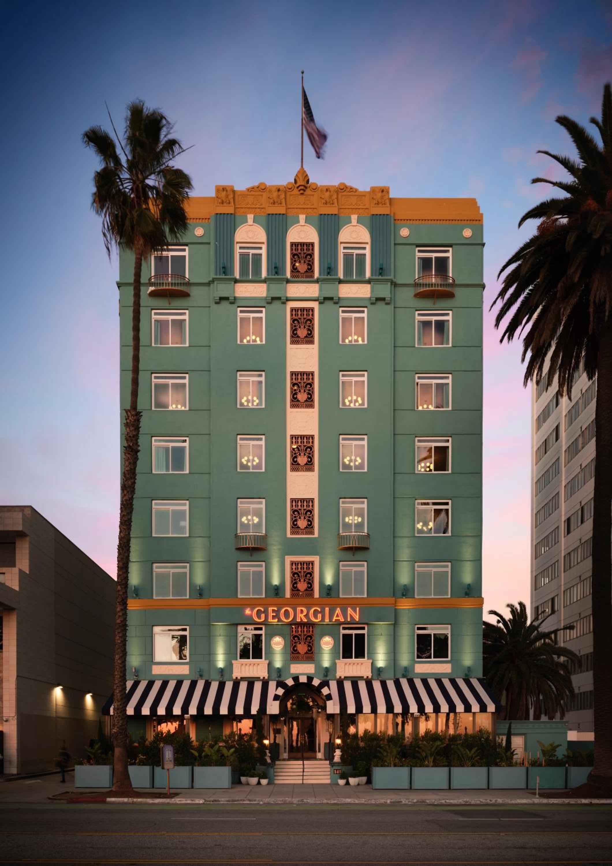 Art Deco elegance meets California cool as this turquoise gem glows against the twilight sky, its striped awnings and palm-lined entrance promising old Hollywood glamour.