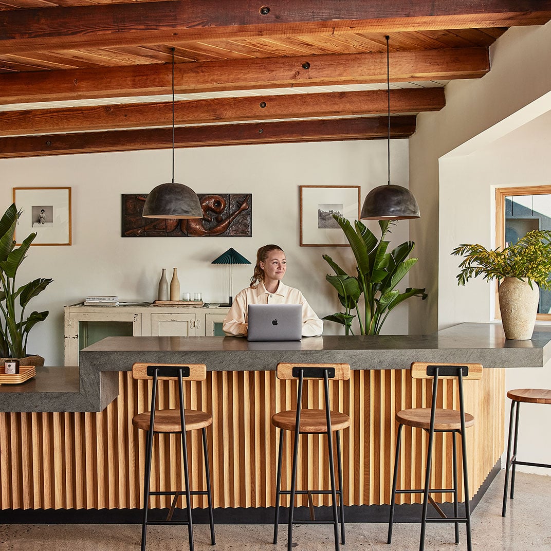 Exposed wooden beams frame a communal workspace where natural textures meet modern functionality, creating an inviting retreat for digital nomads seeking California coastal charm.