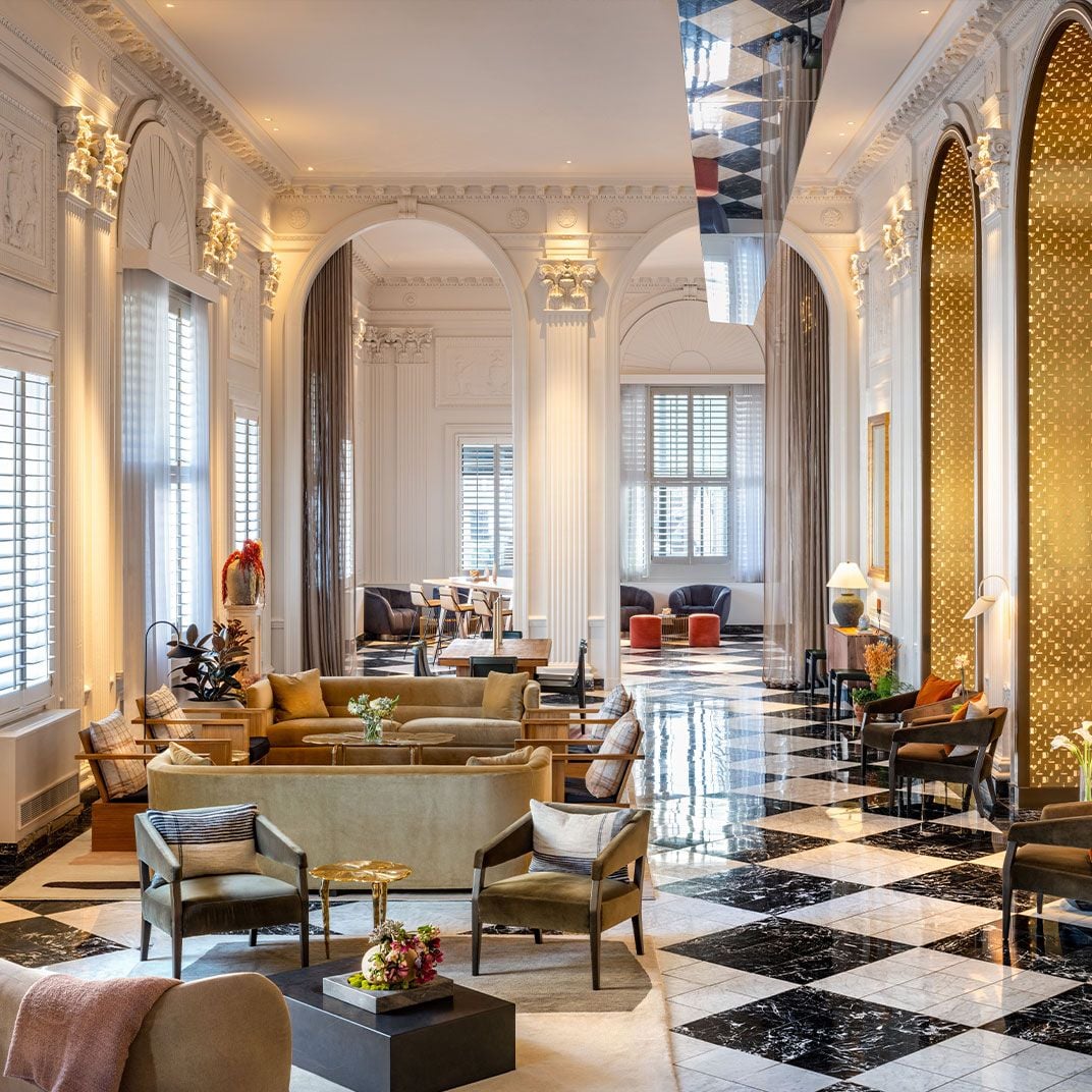 Soaring columns and golden archways frame intimate seating vignettes in this palatial lobby, where checkered marble floors reflect warm light from ornate sconces.