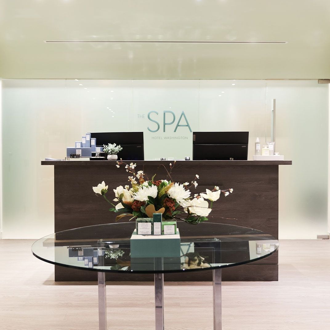 Gleaming glass surfaces and fresh white blooms create a serene sanctuary at the spa reception, where modern minimalism meets thoughtful luxury touches.