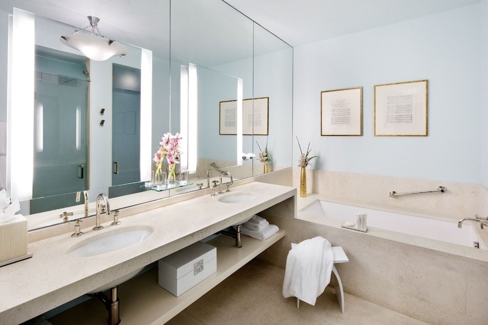Marble surfaces gleam under soft vanity lighting while brass fixtures add warmth to this serene sanctuary, complete with deep soaking tub and thoughtful botanical touches.