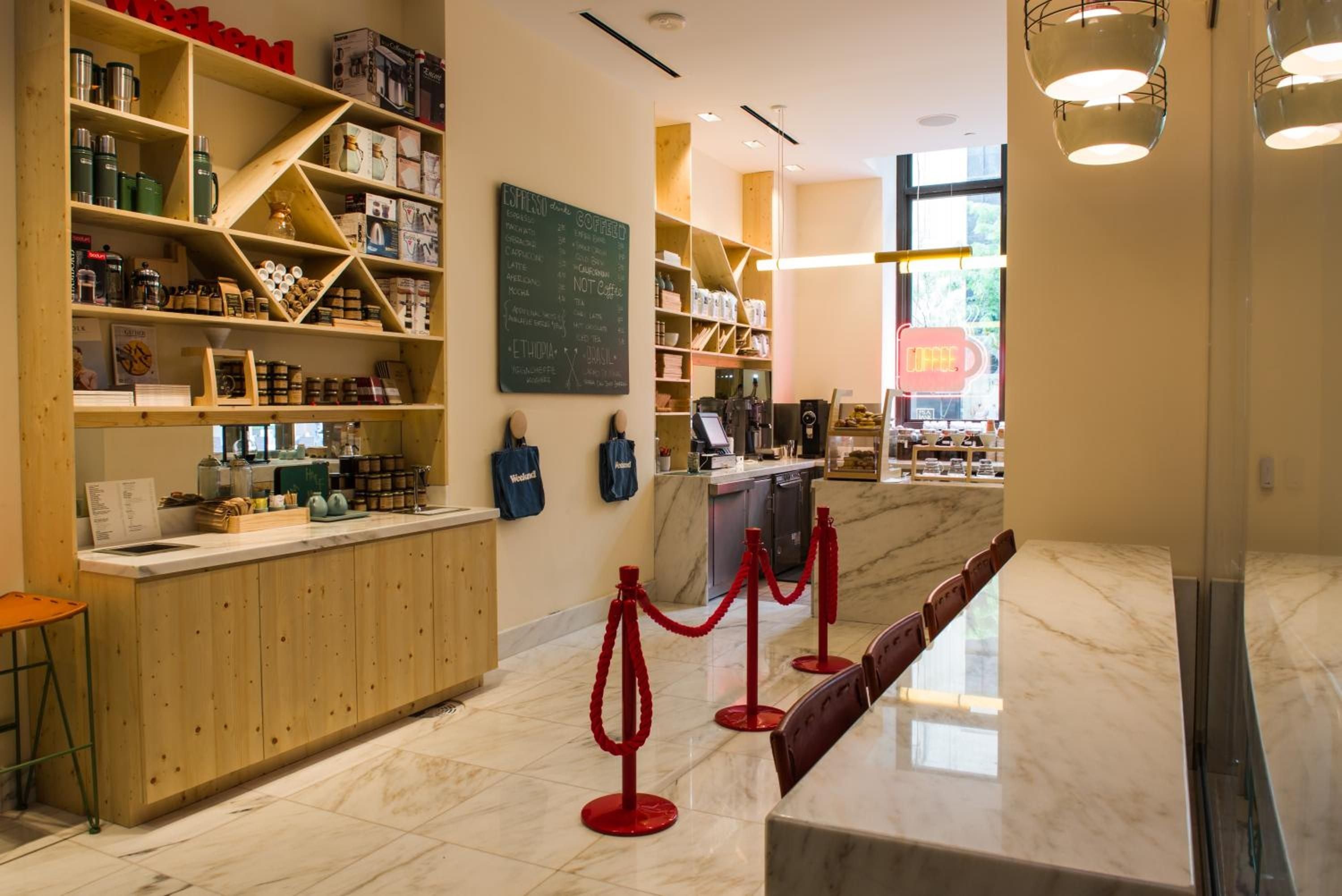 Warm wood shelving displays artisanal goods while red stanchions create an orderly queue in this thoughtfully designed retail space with polished marble floors.