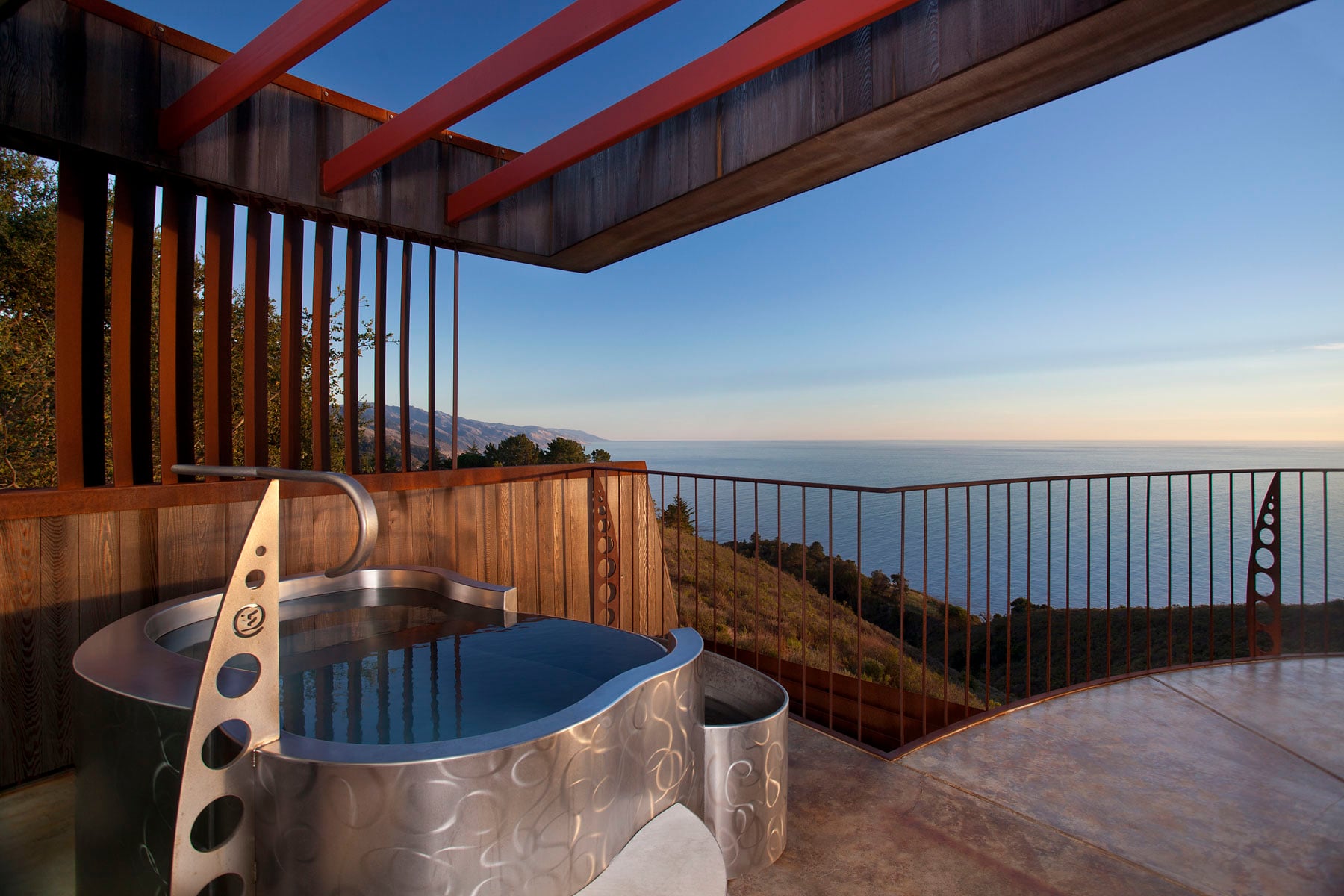 Sculptural steel soaking tub commands the clifftop deck, where redwood beams frame endless Pacific horizons and Big Sur's rugged coastline unfolds below.