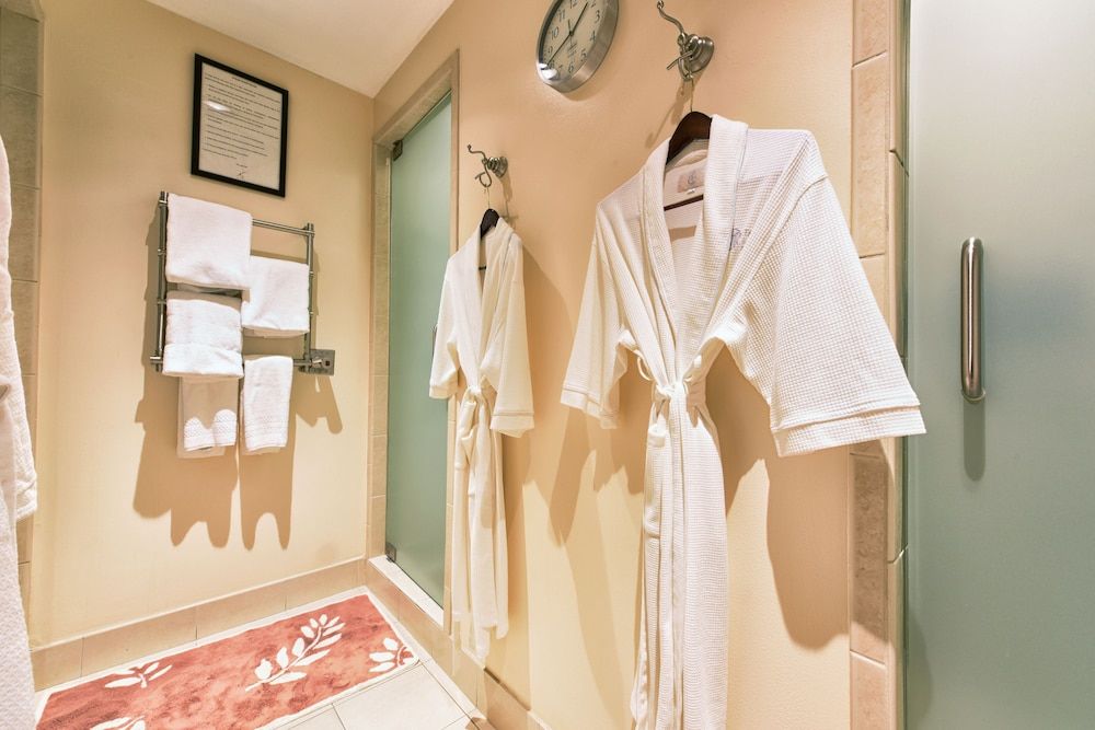 Plush waffle-weave robes hang ready beside warm marble walls, where soft shadows dance across pristine white towels in this intimate spa-like sanctuary.