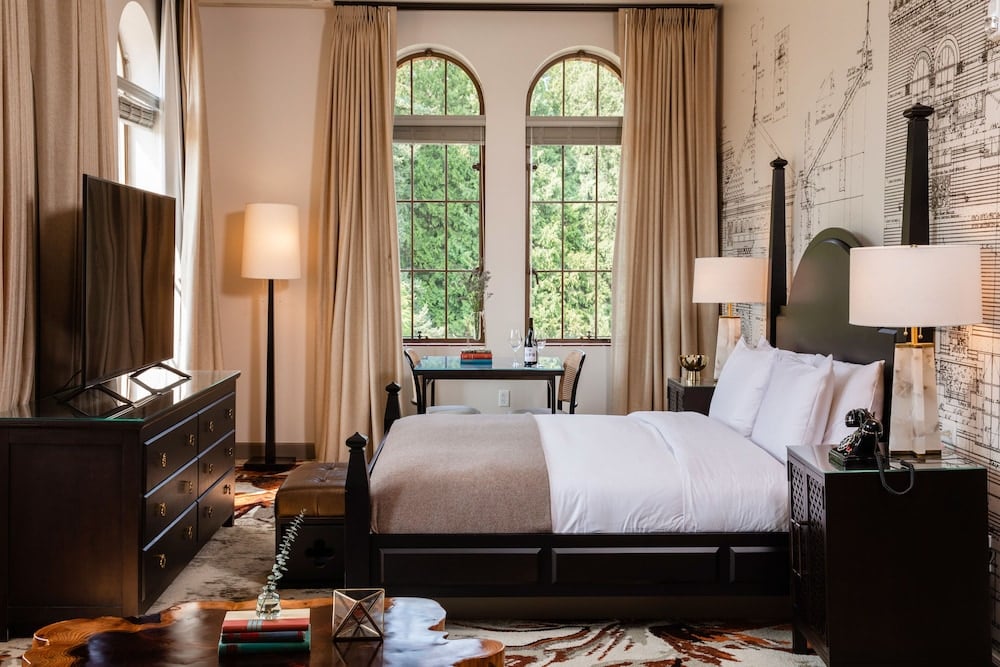 Arched windows frame verdant gardens while historical blueprints adorn walls, creating an intimate sanctuary where monastic heritage meets modern luxury in carefully curated comfort.