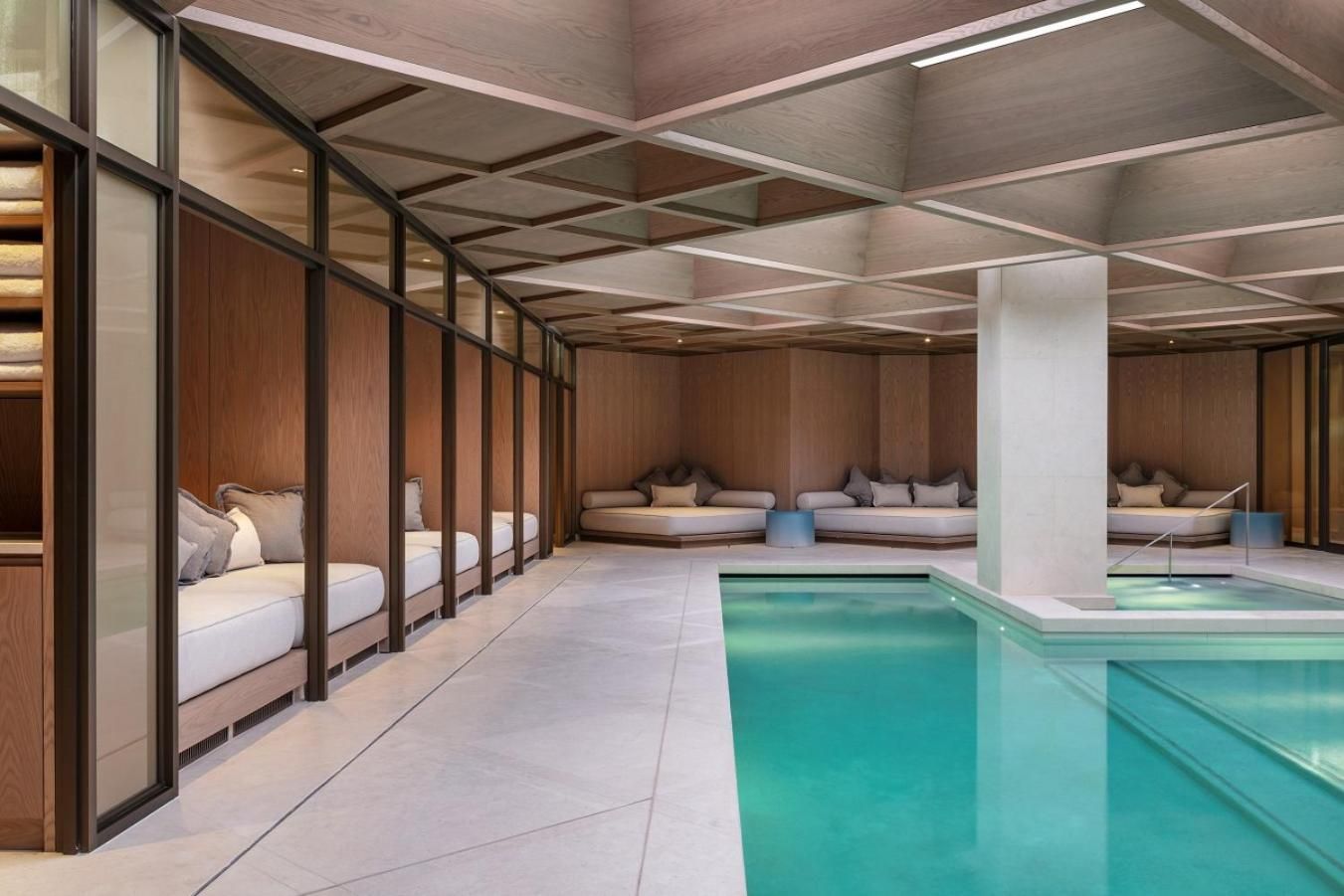 Aquamarine waters glow beneath warm wood paneling and glass pavilions, where plush daybeds invite lingering in this subterranean wellness sanctuary.