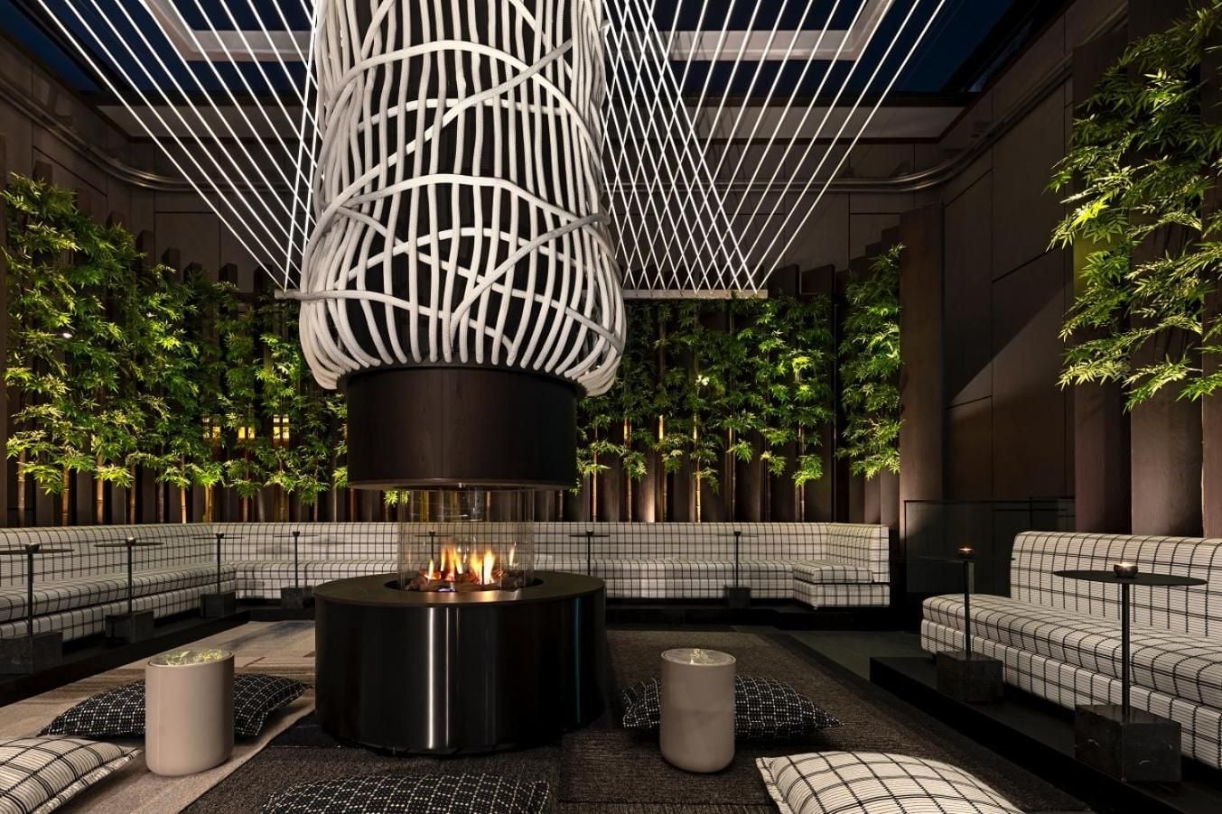 Sculptural white lattice overhead frames intimate seating around a central fire table, where contemporary design meets cozy gathering in this striking atrium lounge.
