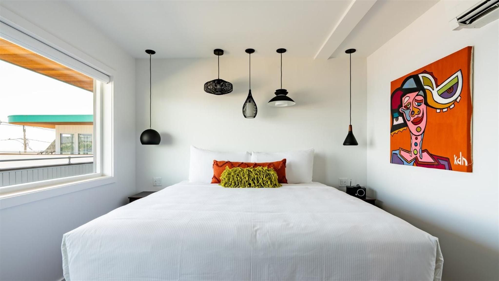 Five distinctive pendant lights create sculptural drama above crisp white linens, while vibrant street art brings playful energy to this thoughtfully curated space.