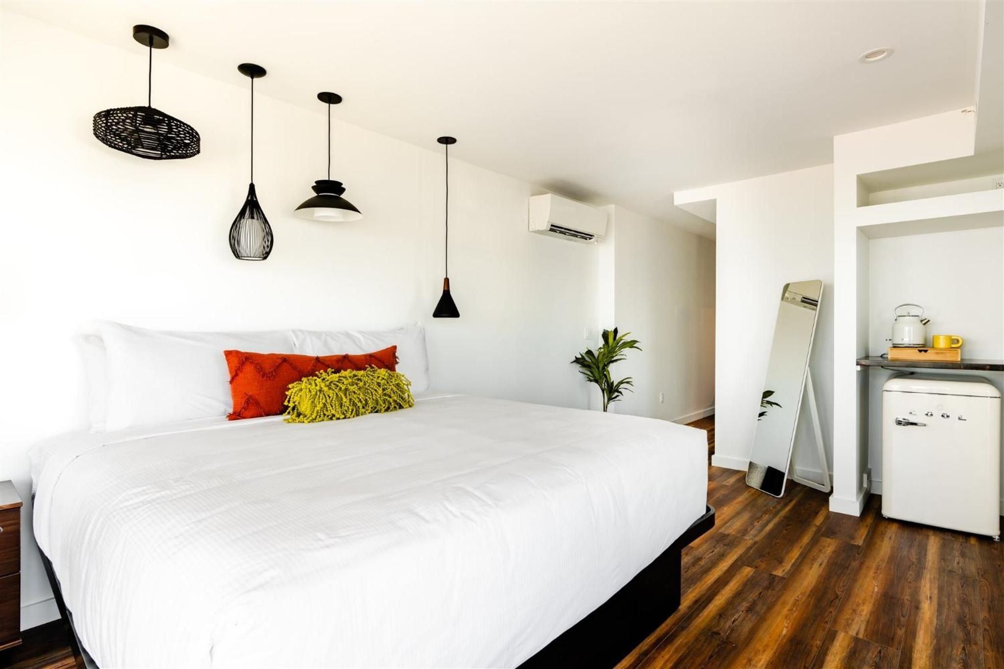 Crisp white linens contrast beautifully with warm hardwood floors, while sculptural black pendant lights and vibrant throw pillows create an inviting studio sanctuary.