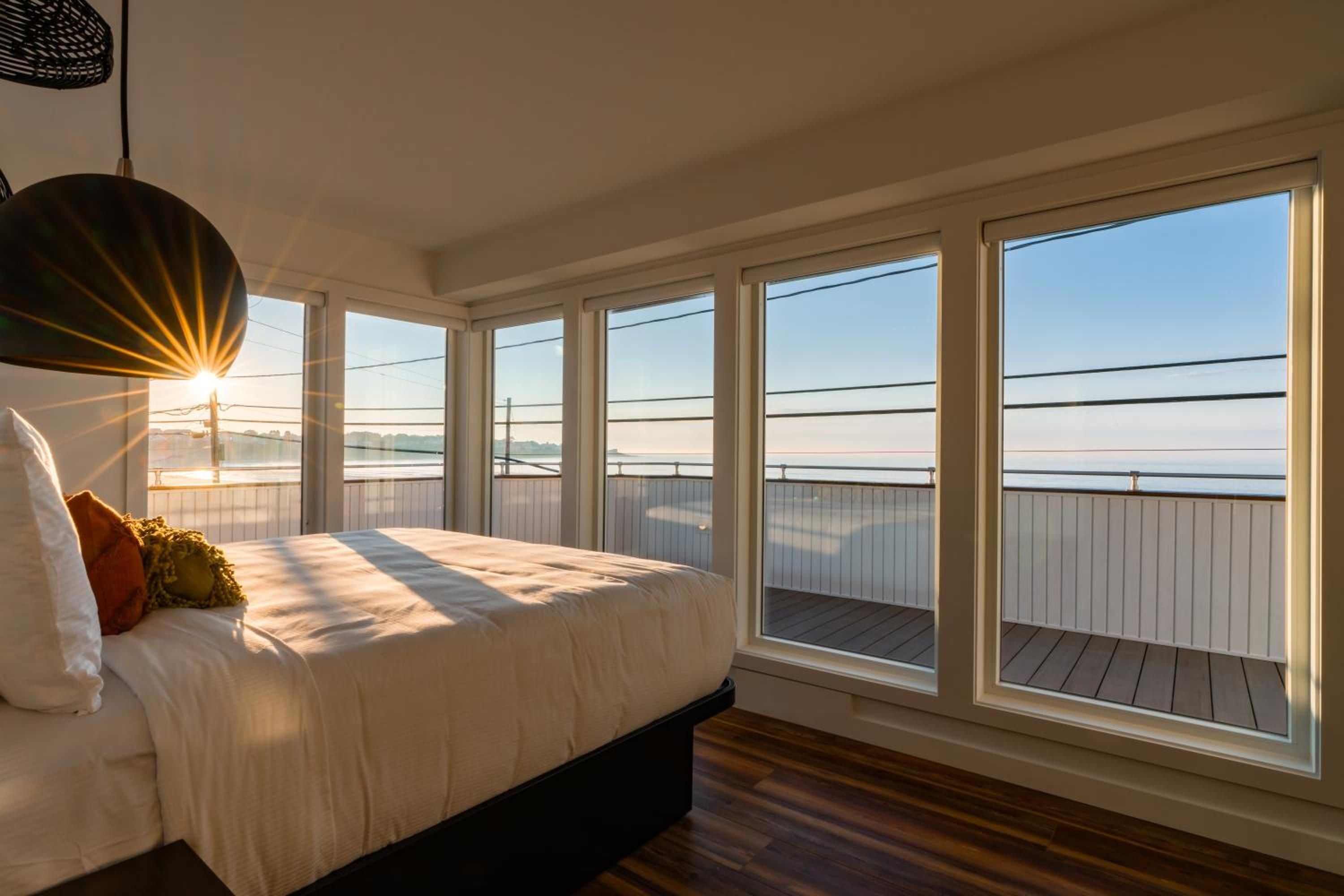 Golden hour light streams through floor-to-ceiling windows, casting dramatic shadows across crisp linens while ocean views stretch toward the horizon beyond the private deck.