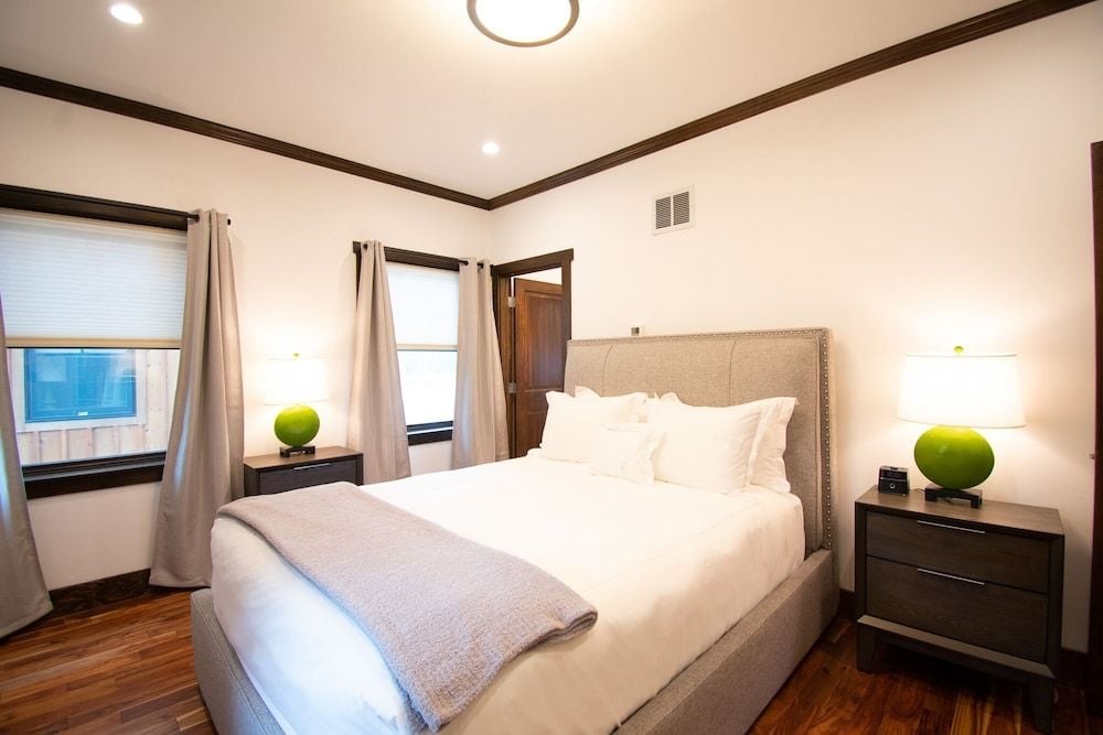Crisp white linens and warm wood floors create a serene retreat, where lime-green accent orbs add playful pops of color to this thoughtfully appointed guest room.
