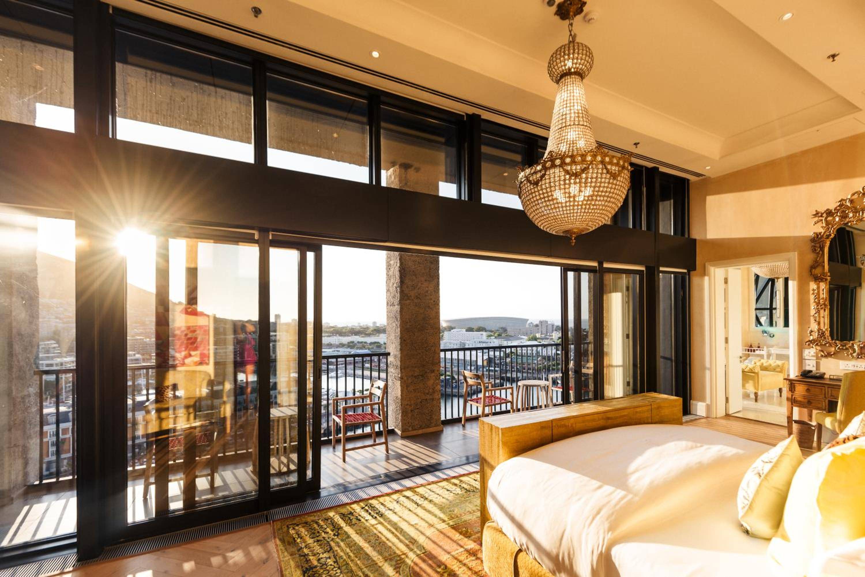 Golden hour light streams through floor-to-ceiling windows in this opulent suite, where crystal chandeliers cast prismatic reflections across polished floors and harbor views stretch beyond.