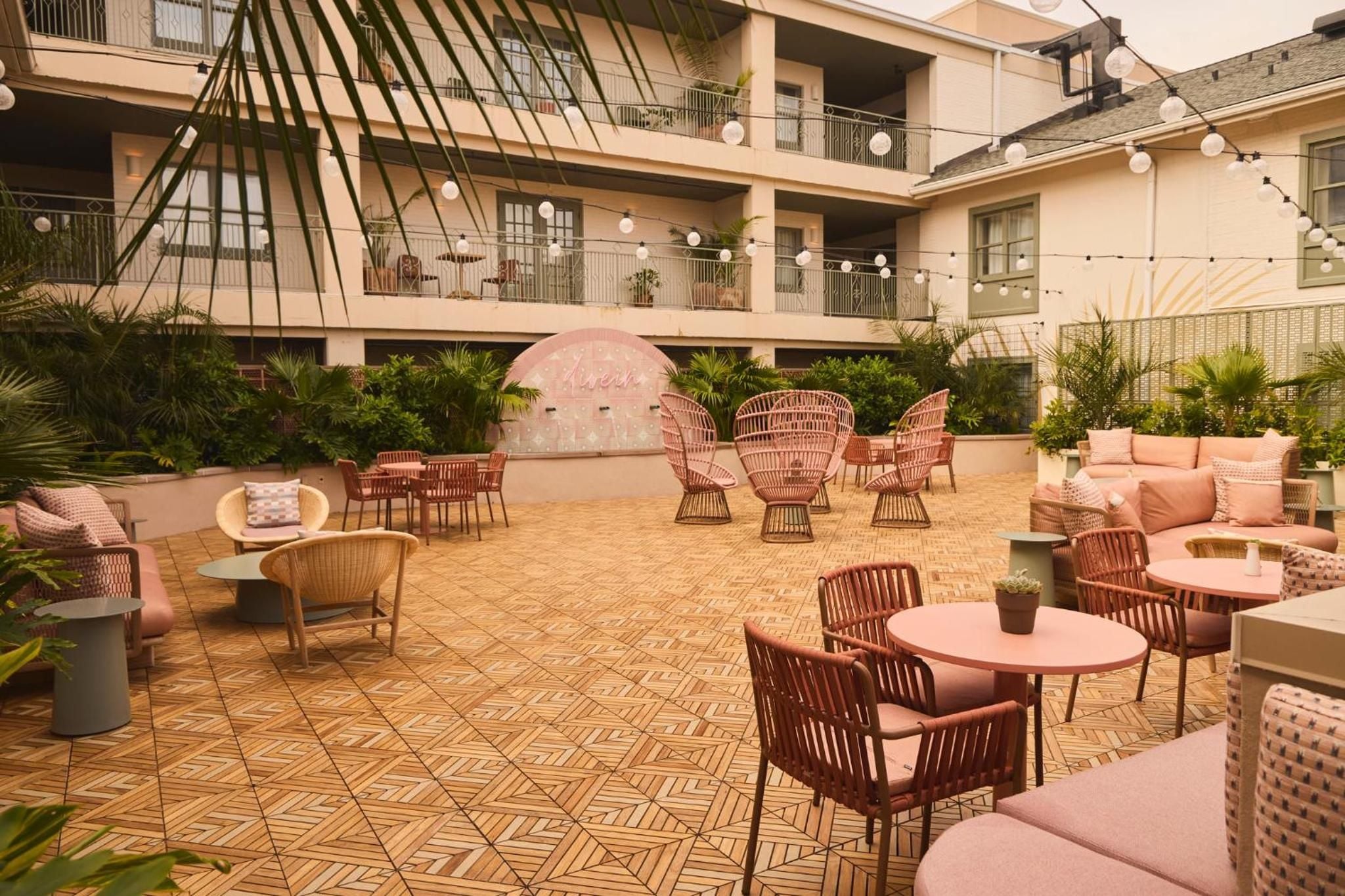 Wicker chairs and coral-pink cushions create intimate seating vignettes on the herringbone-tiled courtyard, where string lights dance overhead between palm fronds.