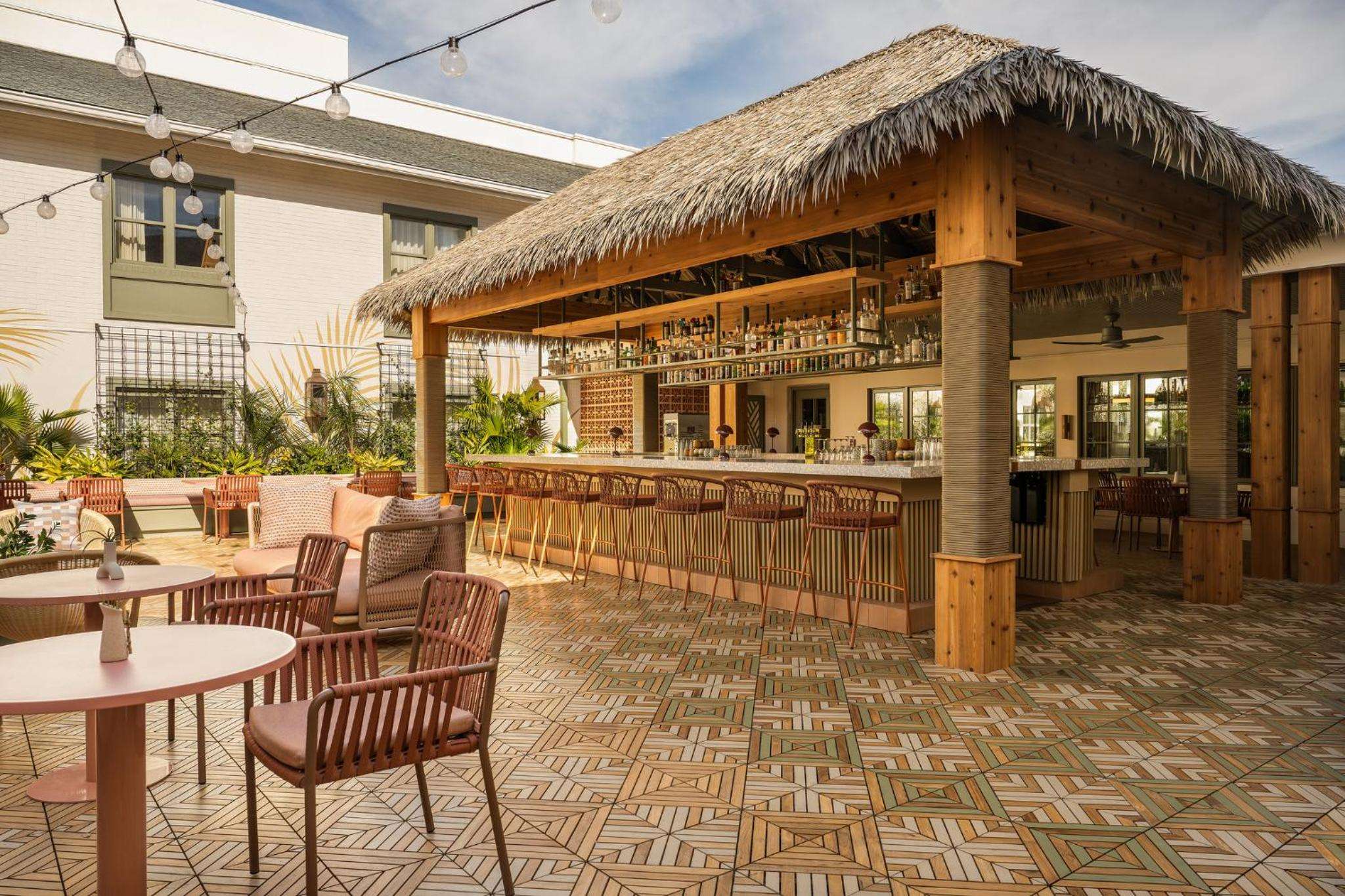 Thatched palapa shelters an inviting rooftop bar where woven chairs and geometric tiles create tropical sophistication beneath string lights and open sky.