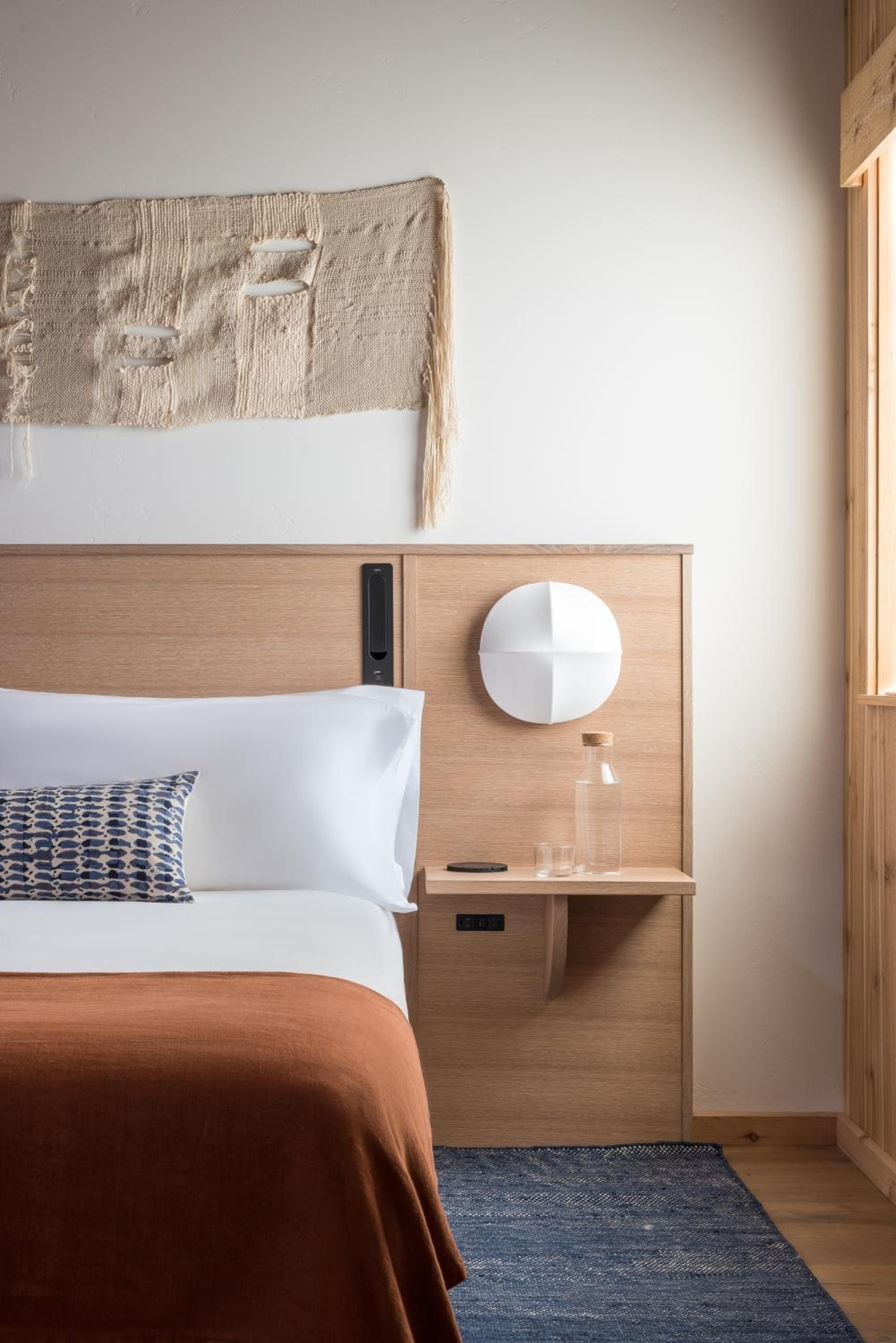 Warm oak built-ins and crisp white linens create a serene sanctuary, where textured wall art and terracotta throws add coastal sophistication to minimalist comfort.