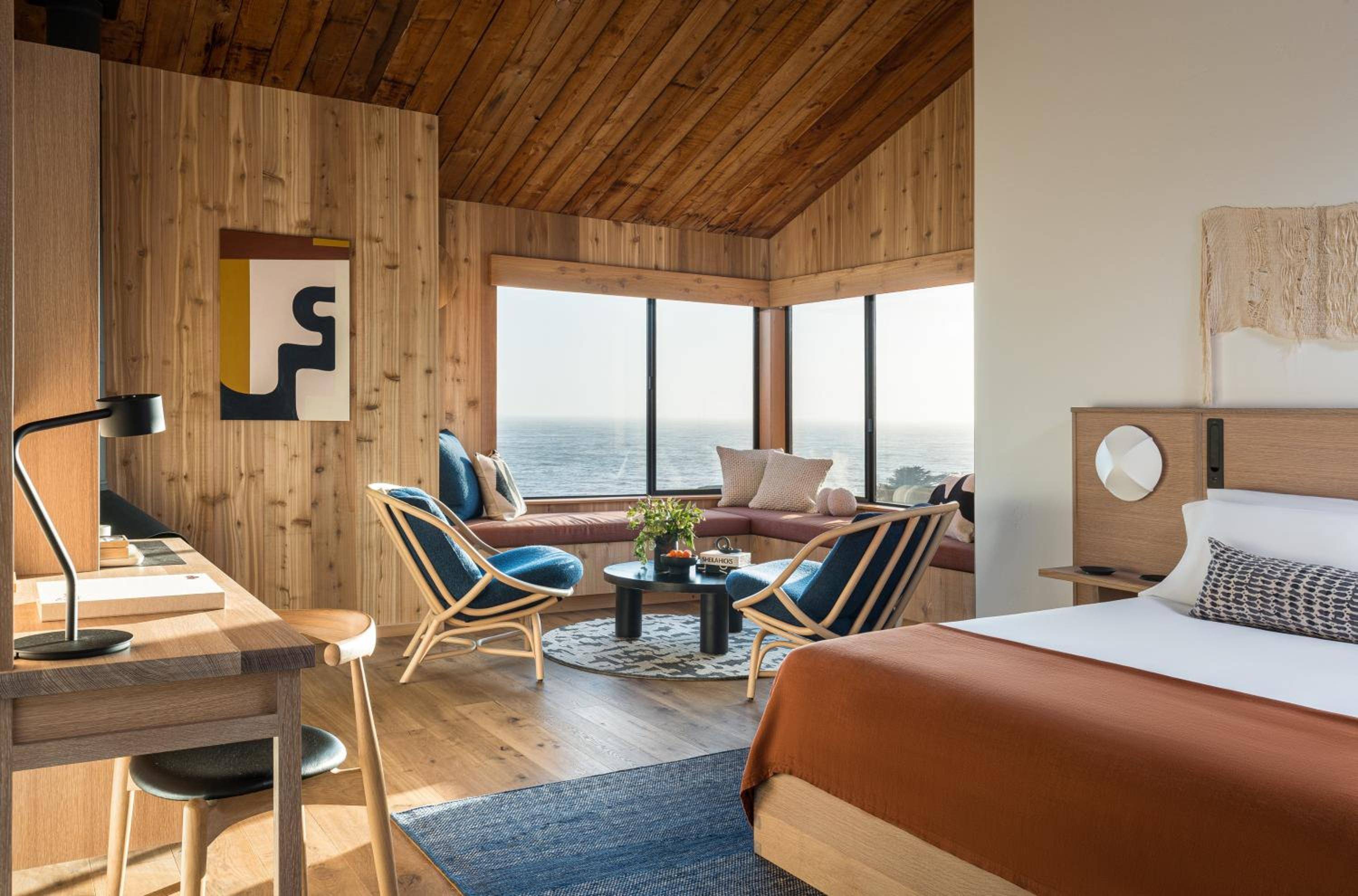 Floor-to-ceiling windows frame endless Pacific views while warm cedar walls and mid-century furnishings create an intimate retreat above California's rugged coastline.