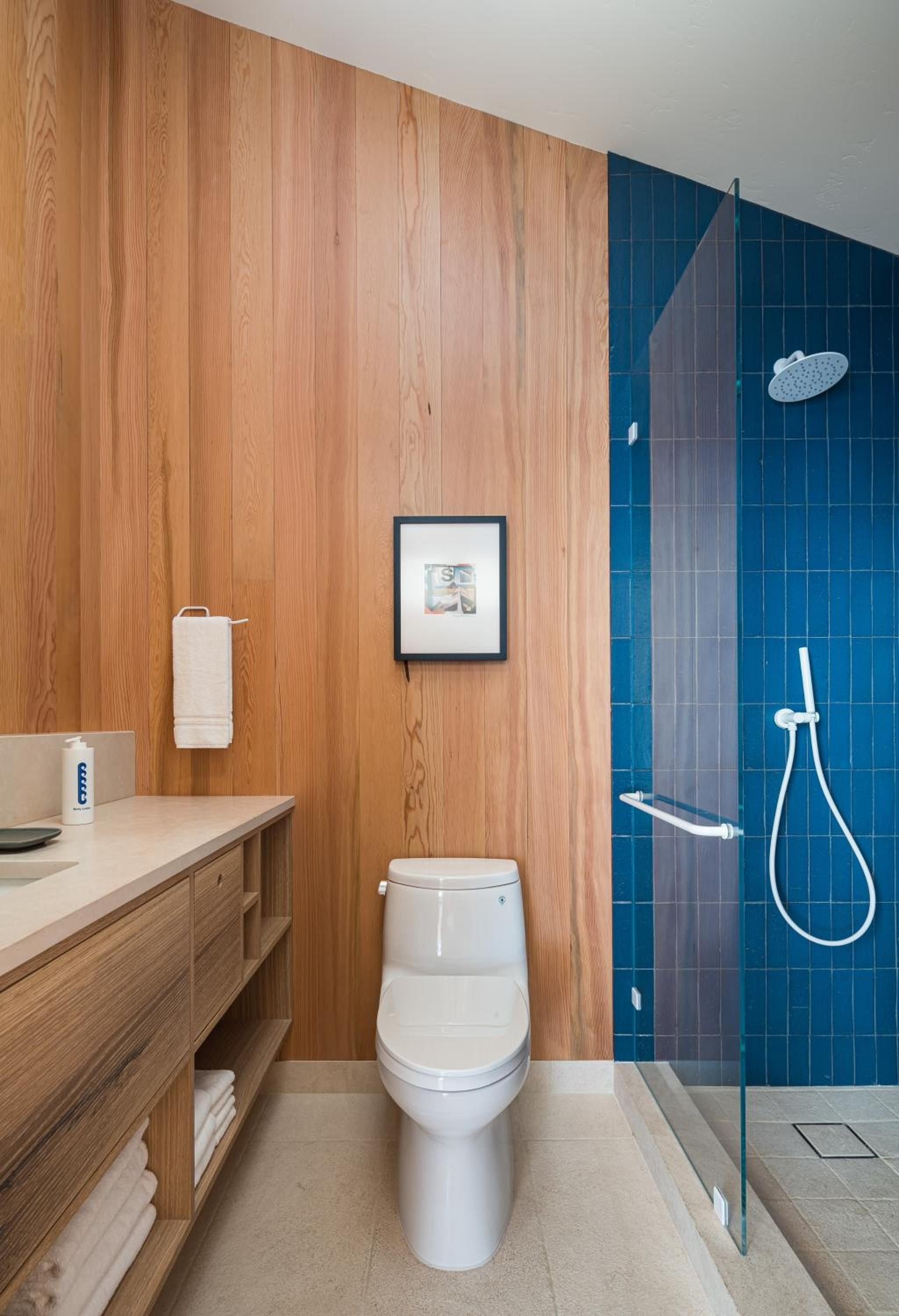 Warm wood paneling meets vibrant cobalt tiles in this sleek sanctuary, where rainfall showers and floating vanities create a serene coastal retreat.