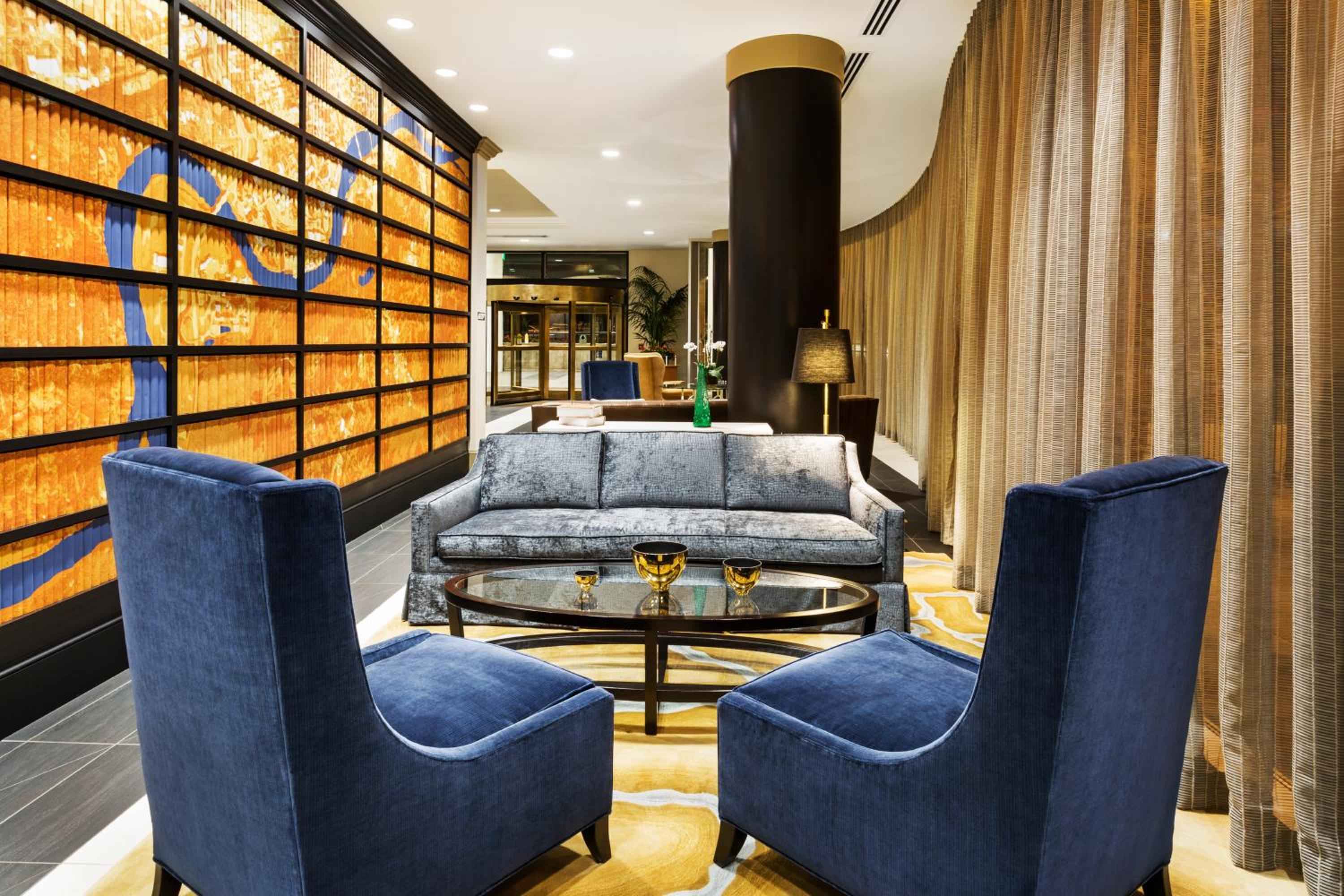 Plush navy velvet armchairs gather around a gleaming coffee table, while honeyed wood panels cast warm geometric shadows across this inviting conversation nook.