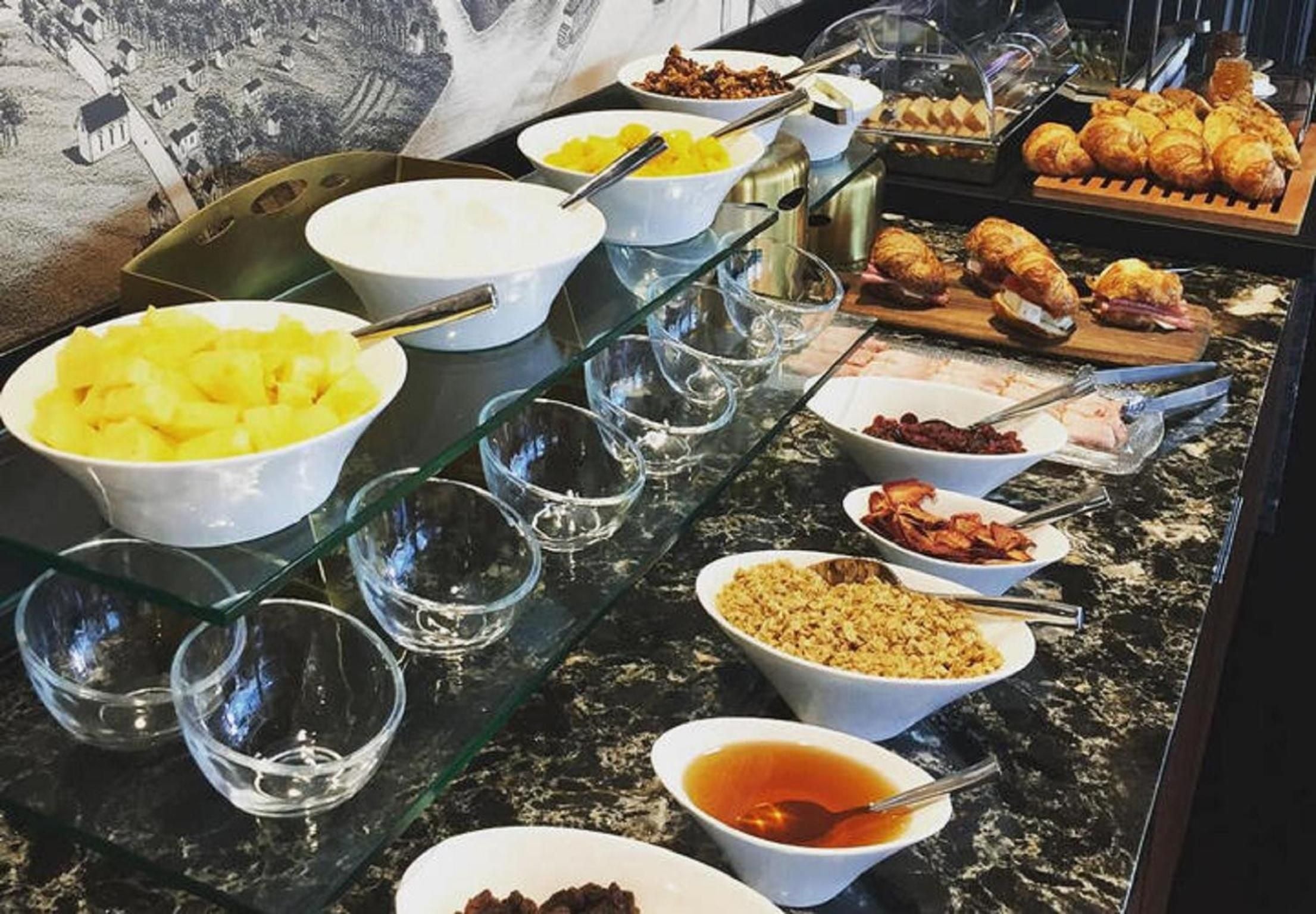 Morning light illuminates a thoughtfully curated breakfast spread featuring fresh pineapple, artisanal pastries, and house-made preserves arranged on gleaming marble countertops.