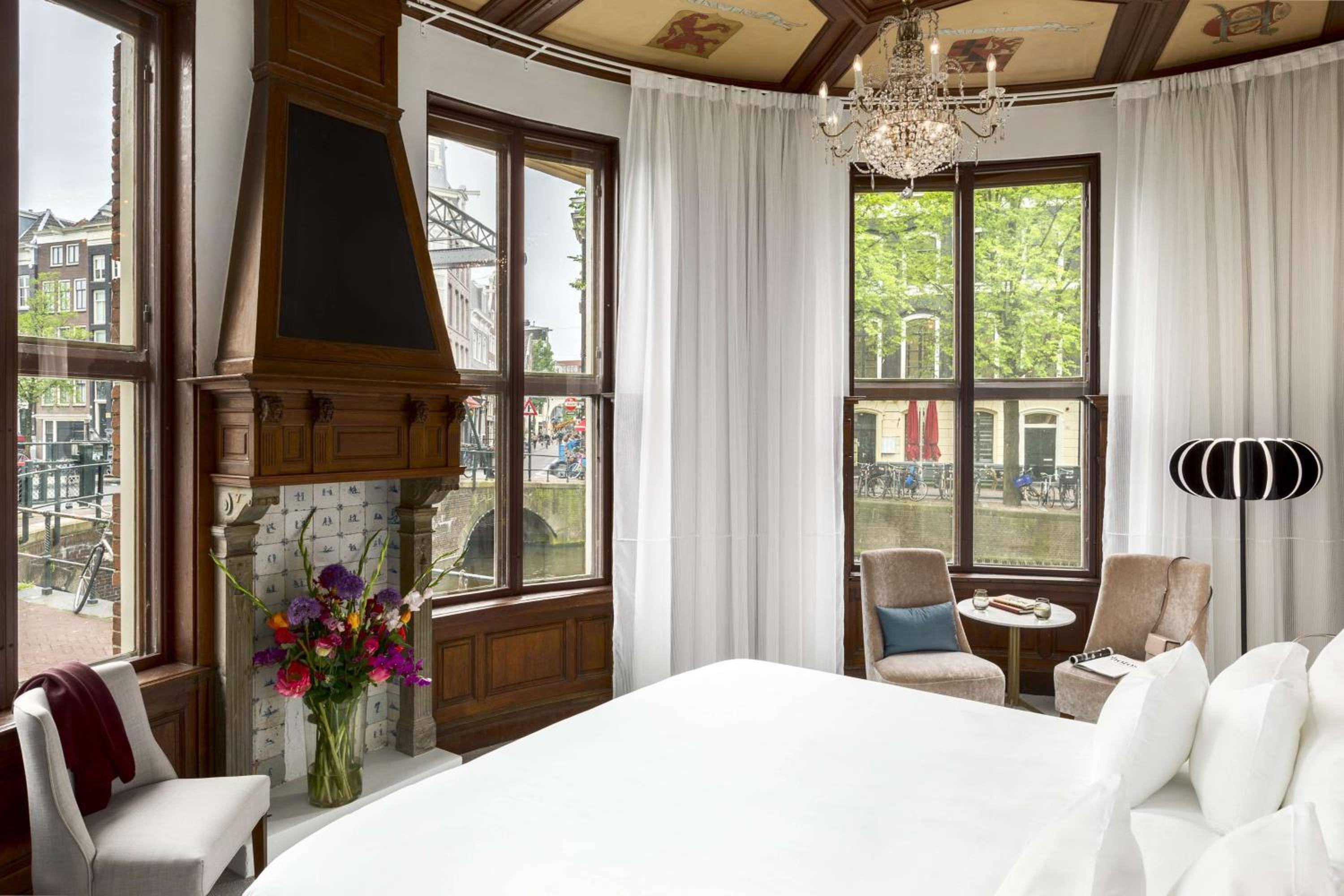 Corner windows frame Amsterdam's historic canals from this elegant suite, where rich wood paneling and crystal chandeliers create an intimate sanctuary above the waterways.