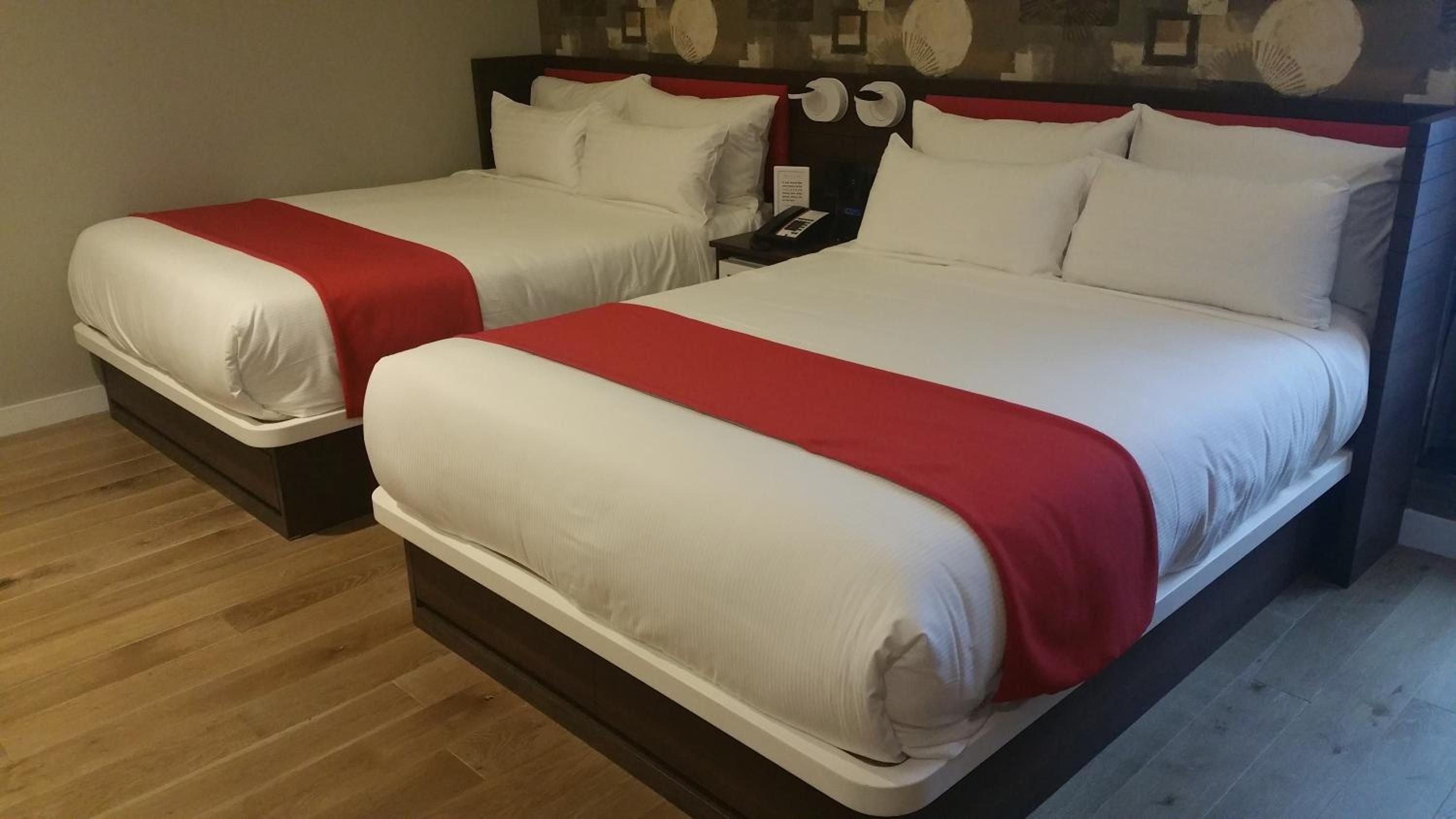 Clean lines and bold red accents define these twin platform beds, where modern minimalism meets thoughtful comfort on warm hardwood floors.