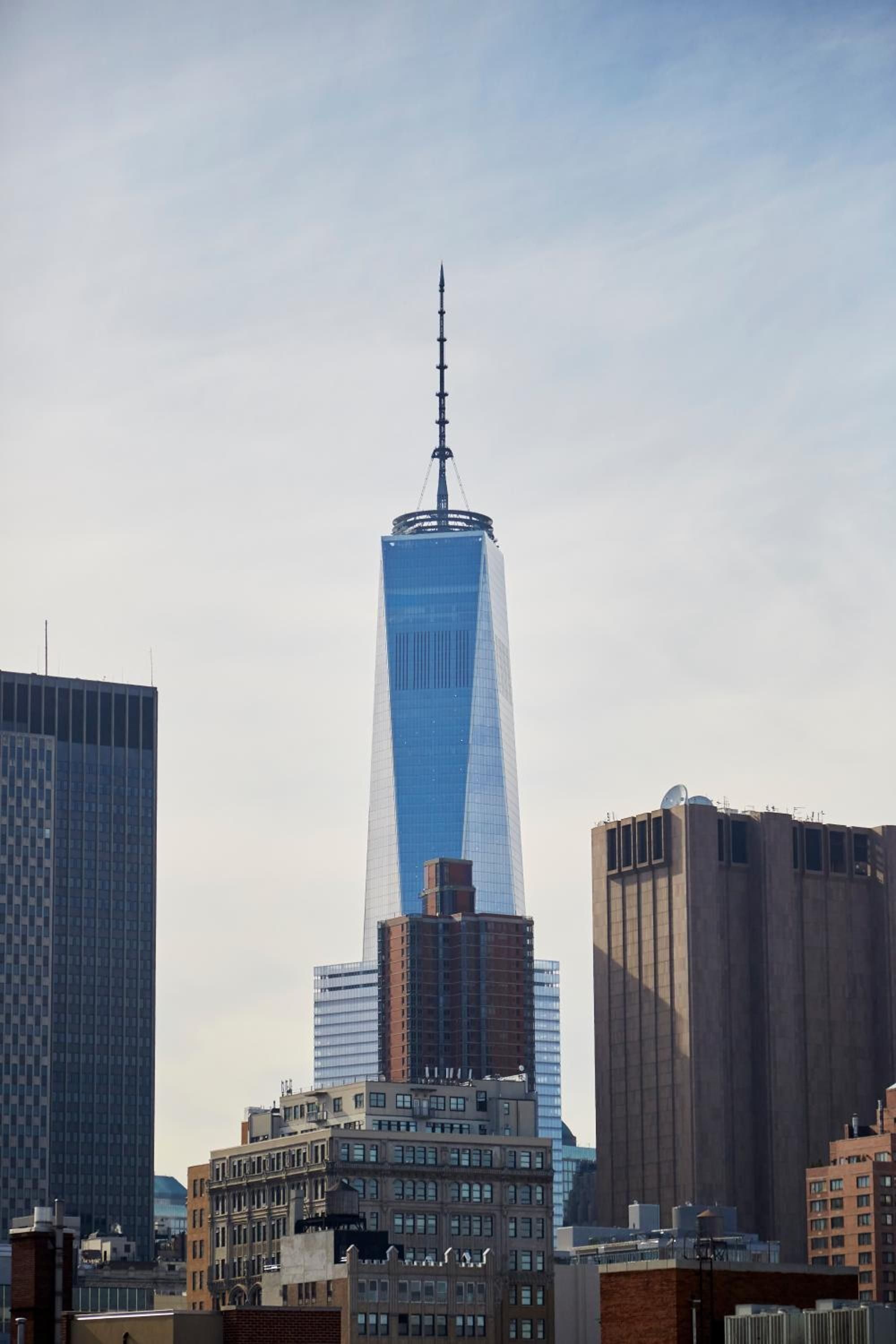 One World Trade Center pierces the Manhattan skyline from your room, its gleaming glass facade catching afternoon light above the dense urban tapestry below.
